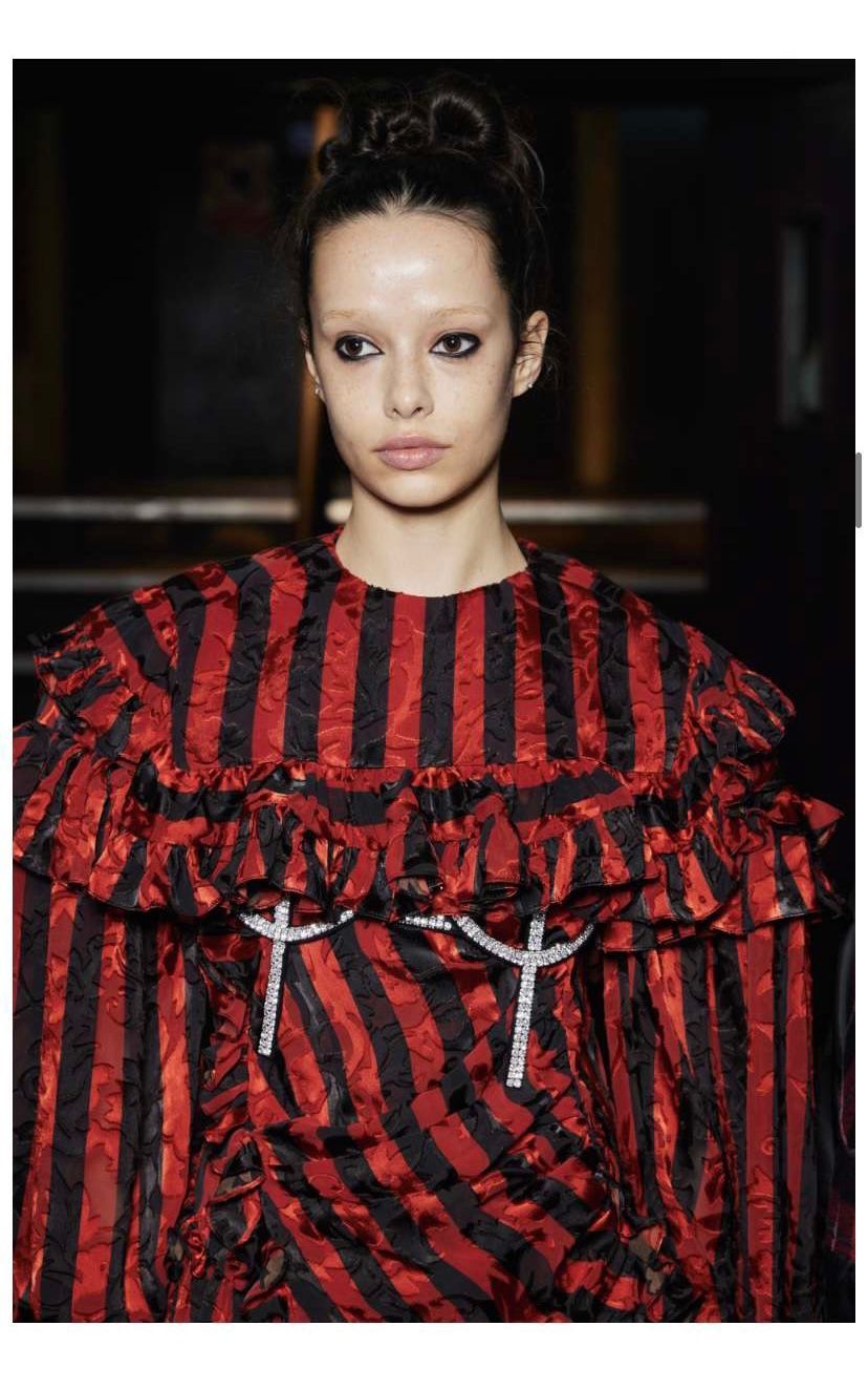 Model in a red and black striped dress with ruffles and jeweled accents; dark setting.