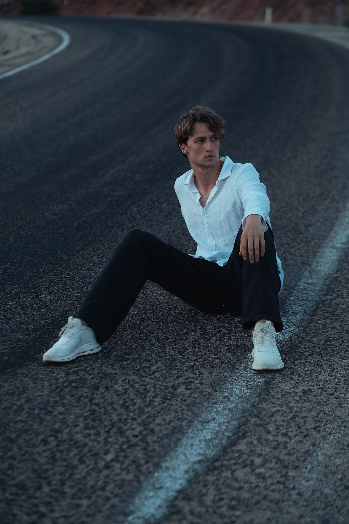 Man in white shirt and black pants sits on a road.