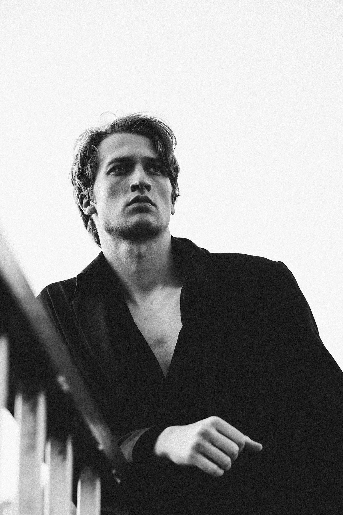 Man leaning on a railing, gazing upward. Wearing a dark open shirt. Black and white.