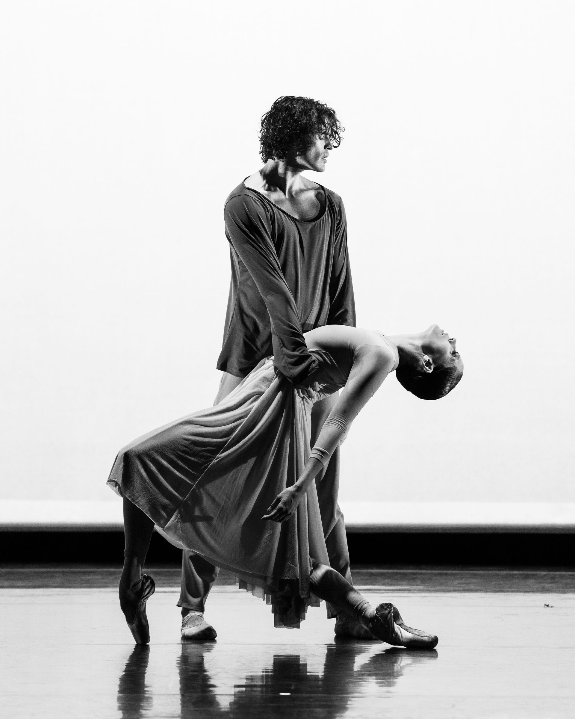 Ballet dancers in a performance. Woman arched back in flowing dress, man supporting her. Black and white, stage setting.