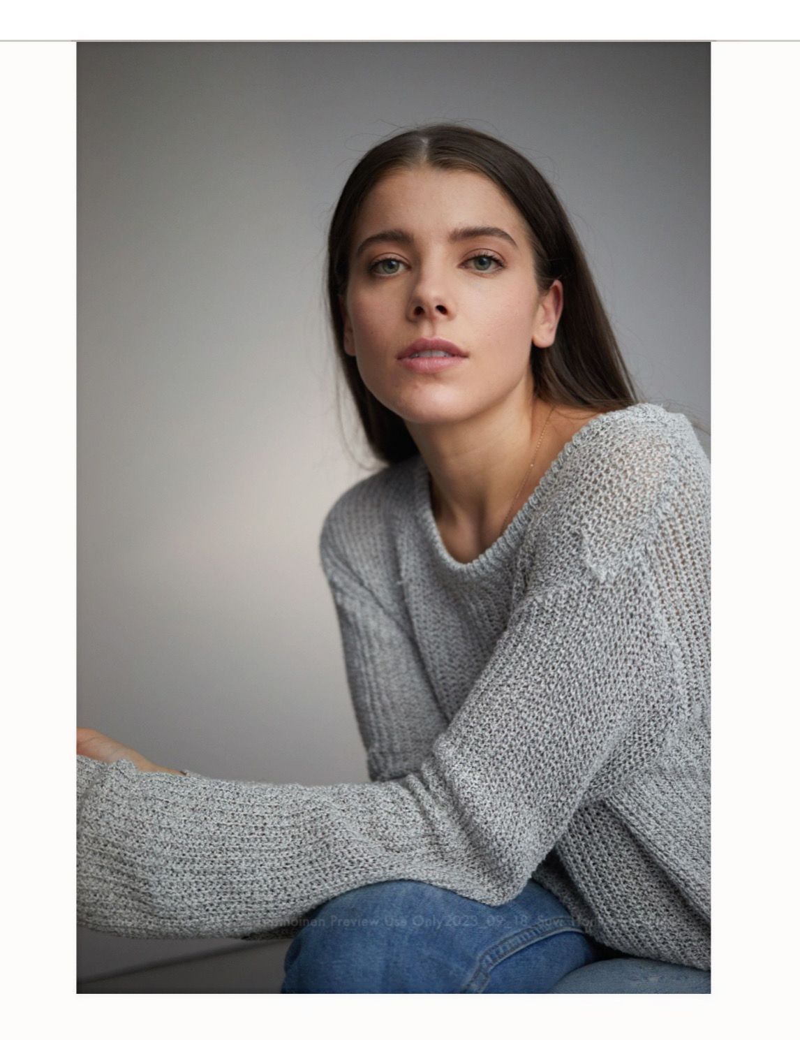 Woman in a gray sweater and blue jeans, looking at the camera. Neutral background.