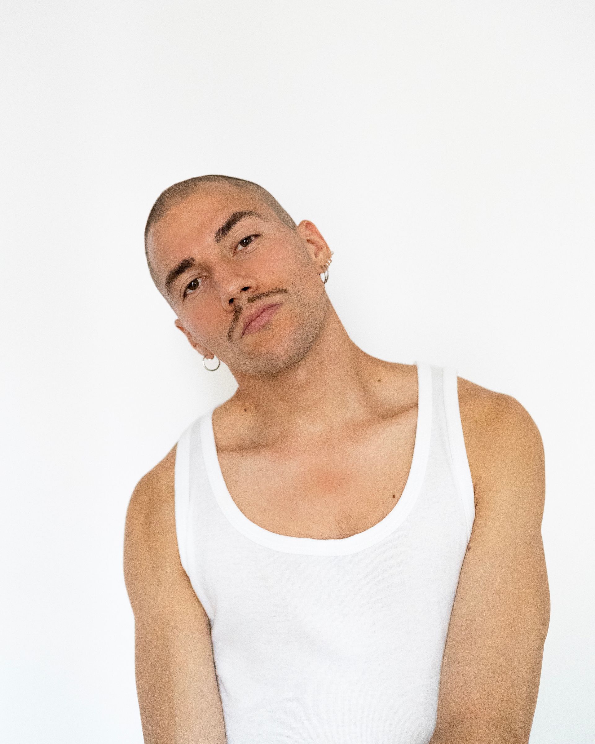 Man in white tank top, head tilted, looking slightly down. White background.