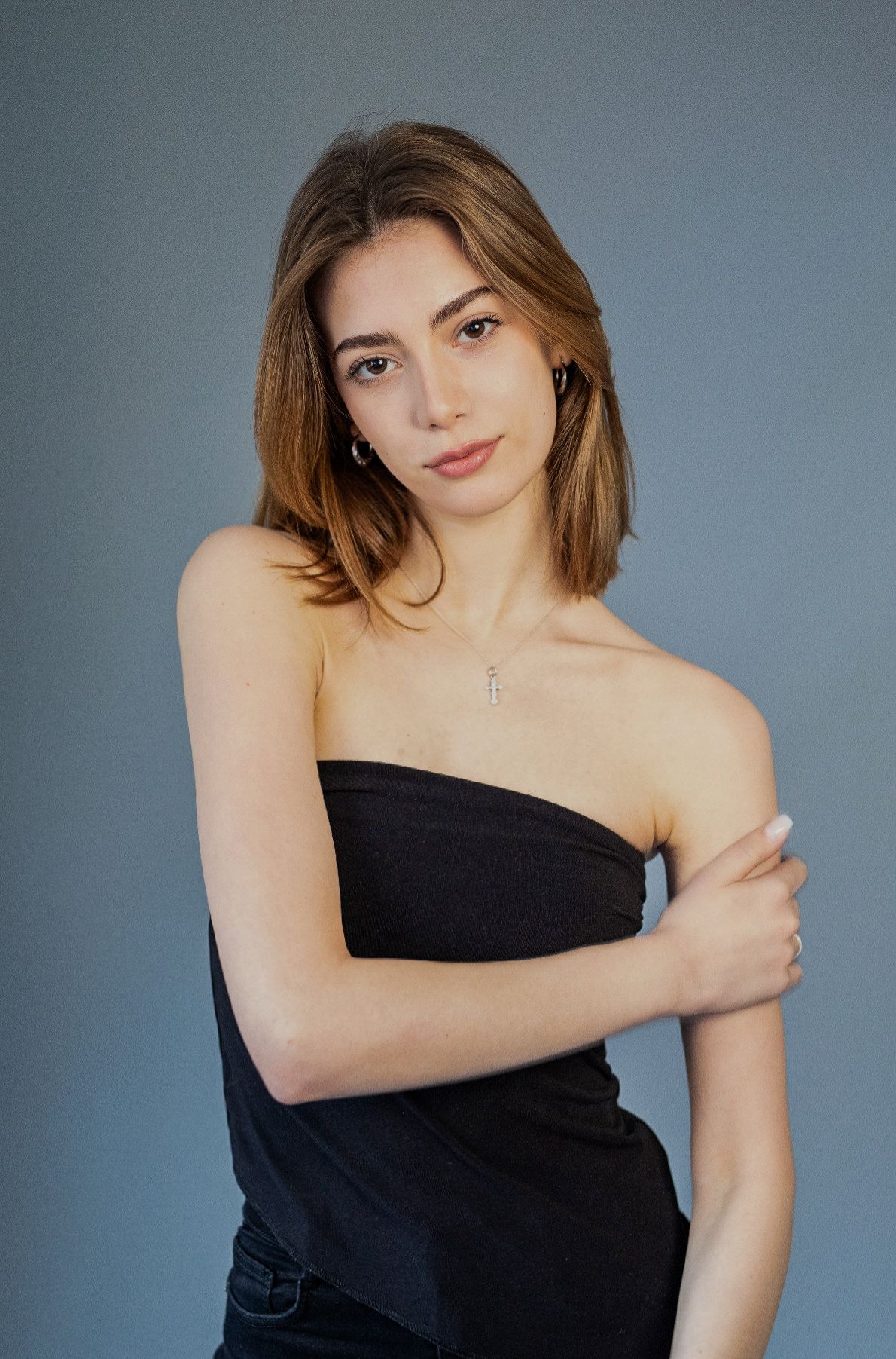 Woman in black strapless top, arms crossed, looking at the camera against a gray backdrop.