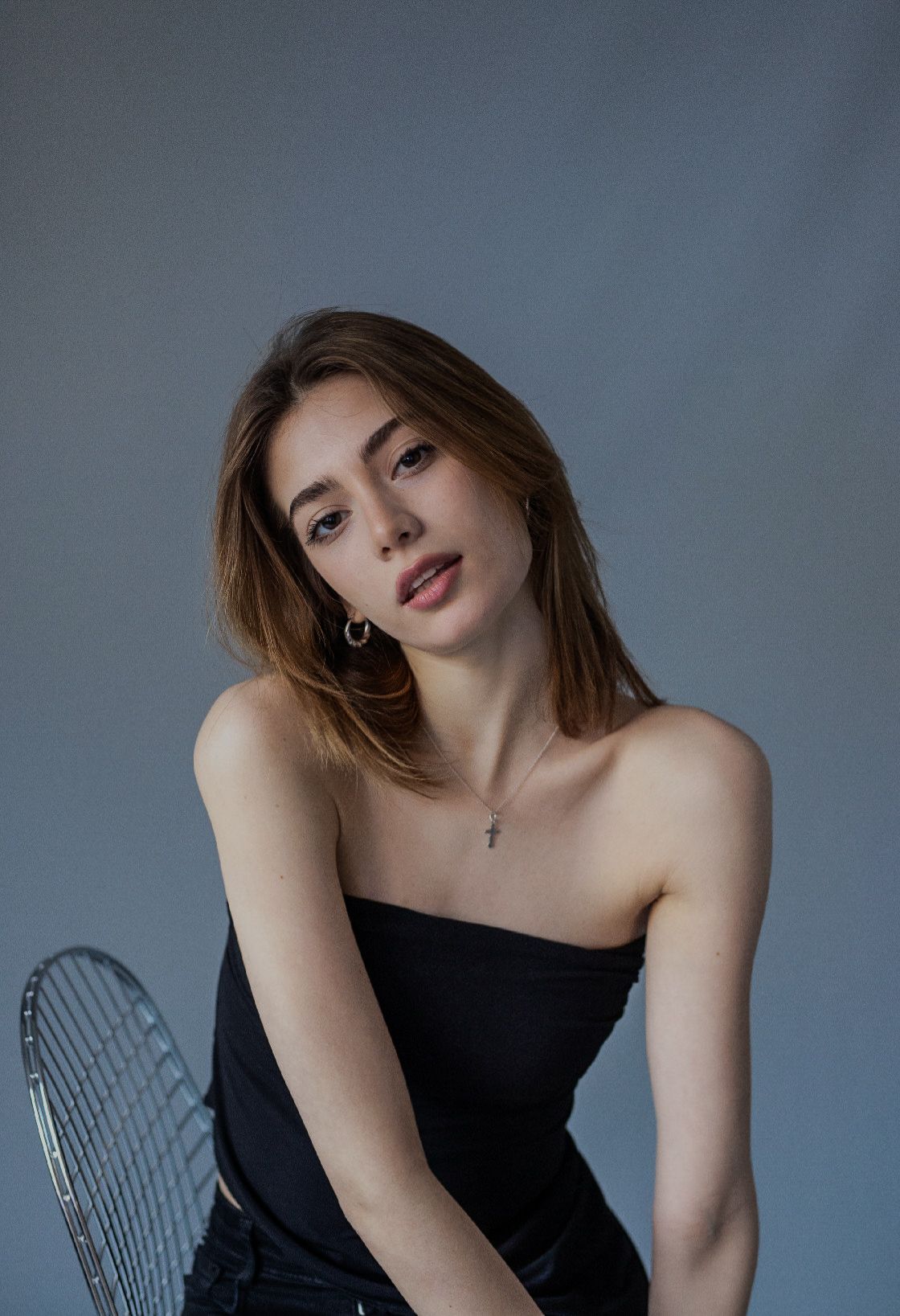 Woman in black tube top, head tilted, looking towards the camera, sitting.