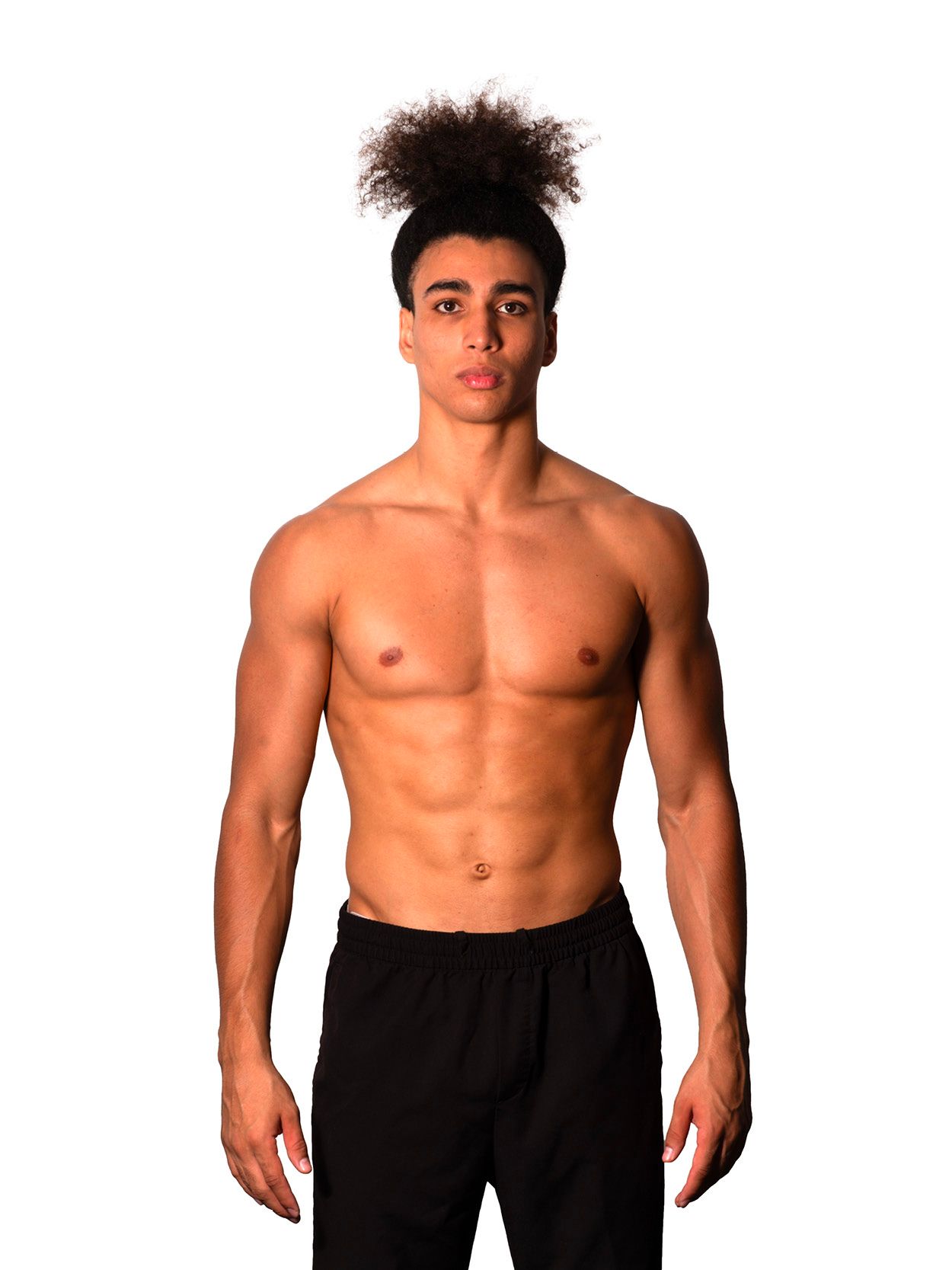 Bare-chested person with dark, curly hair and black pants stands against a white background.