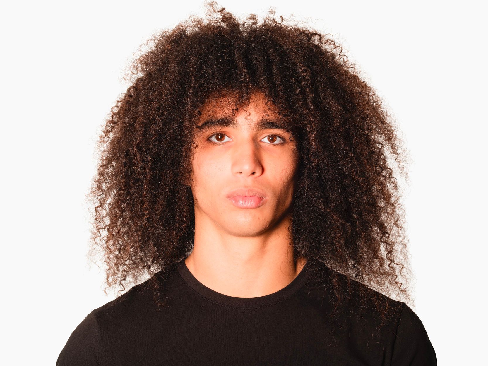 Man with voluminous curly hair and a black shirt against a white background.