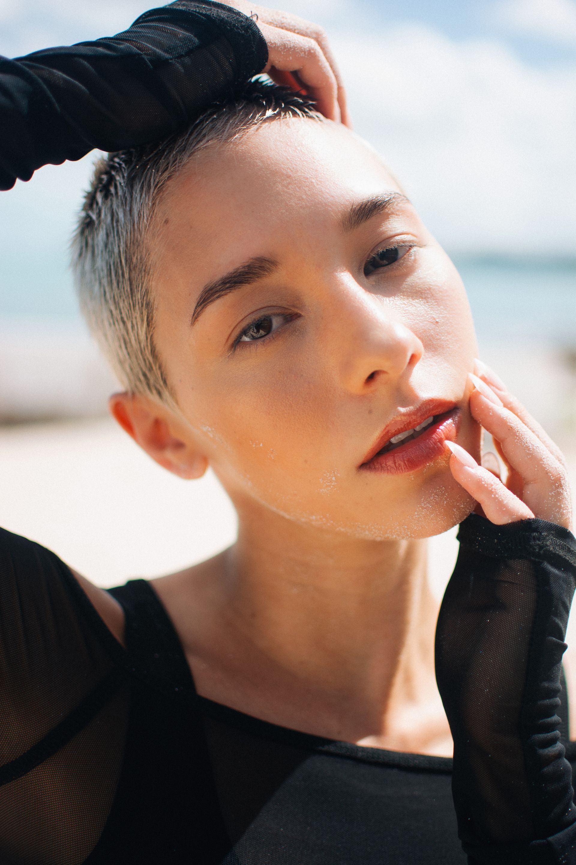 Woman with short gray hair, hand on face, beach setting.