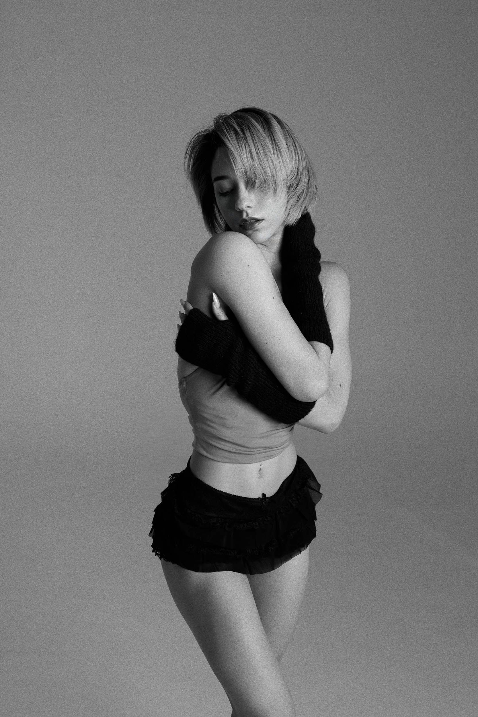 Woman in black shorts and arm warmers, arms crossed, head tilted down. Black and white.