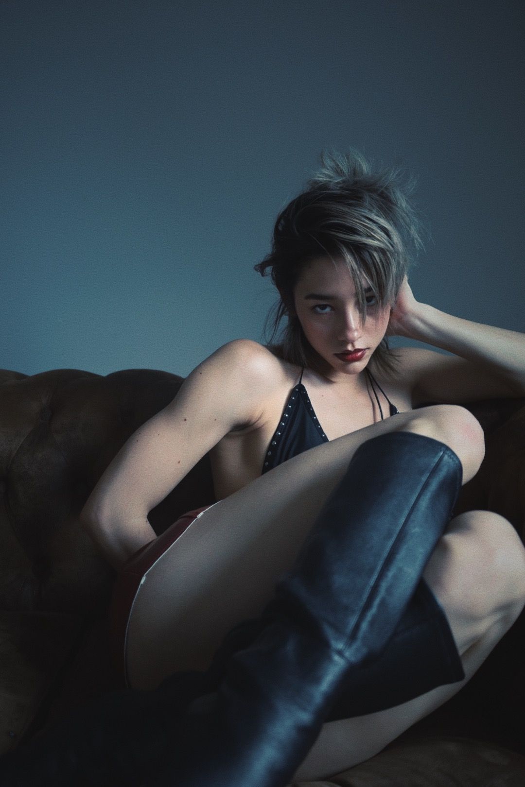 Woman in black halter top and boots, sitting on a brown couch.