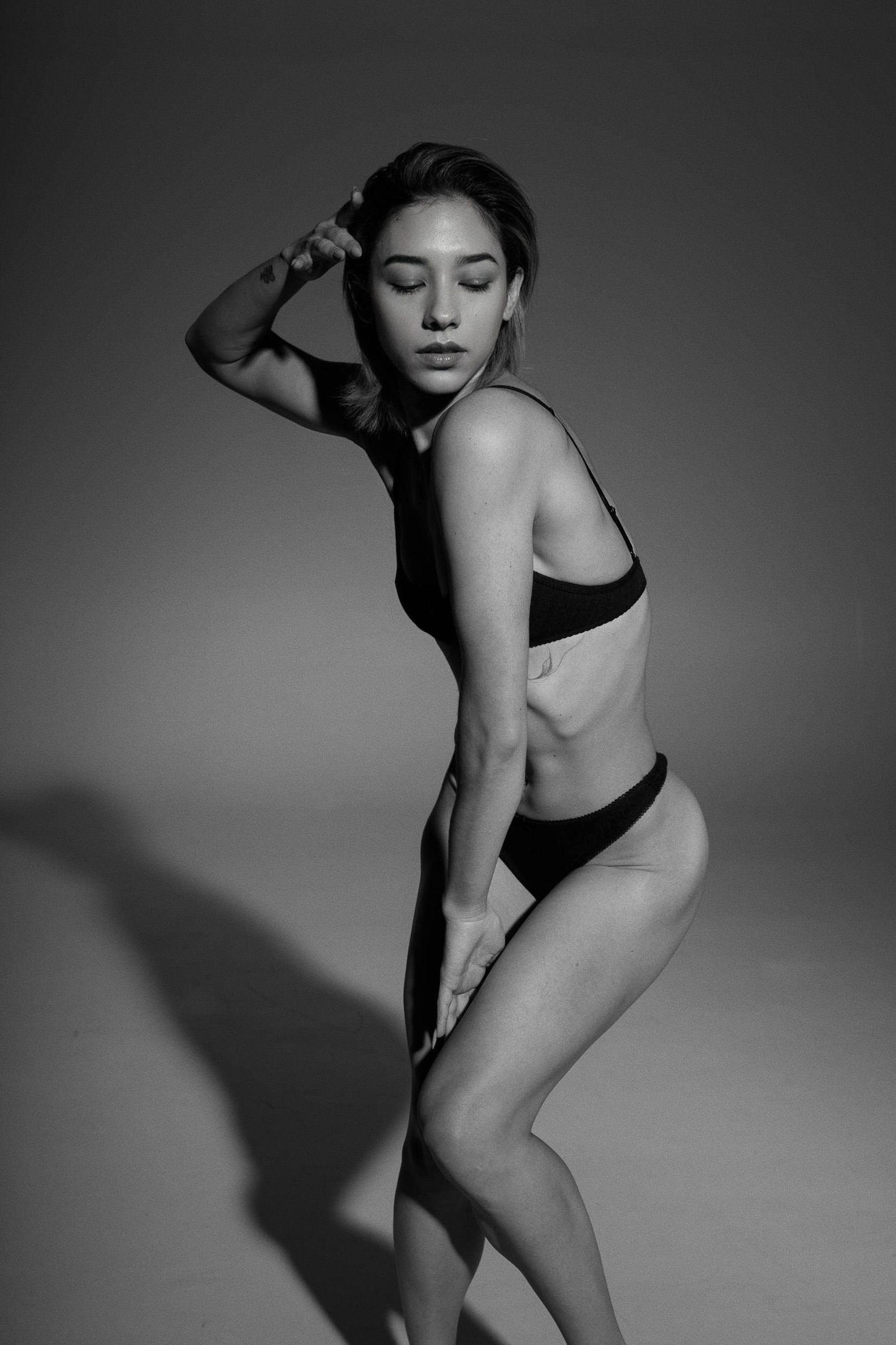 Woman in black lingerie posing, hand on head, in a studio with a shadow.