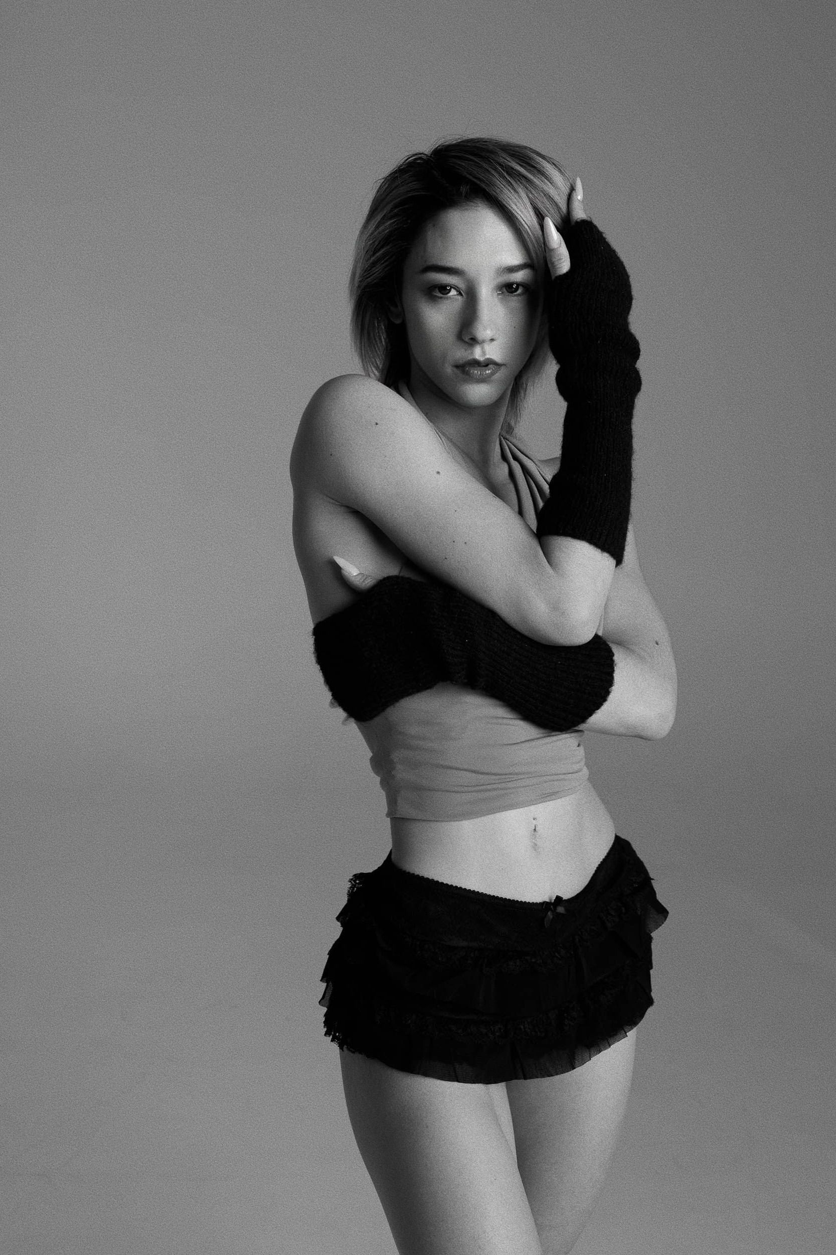 Woman in black tube top, arm warmers, and skirt, posing.