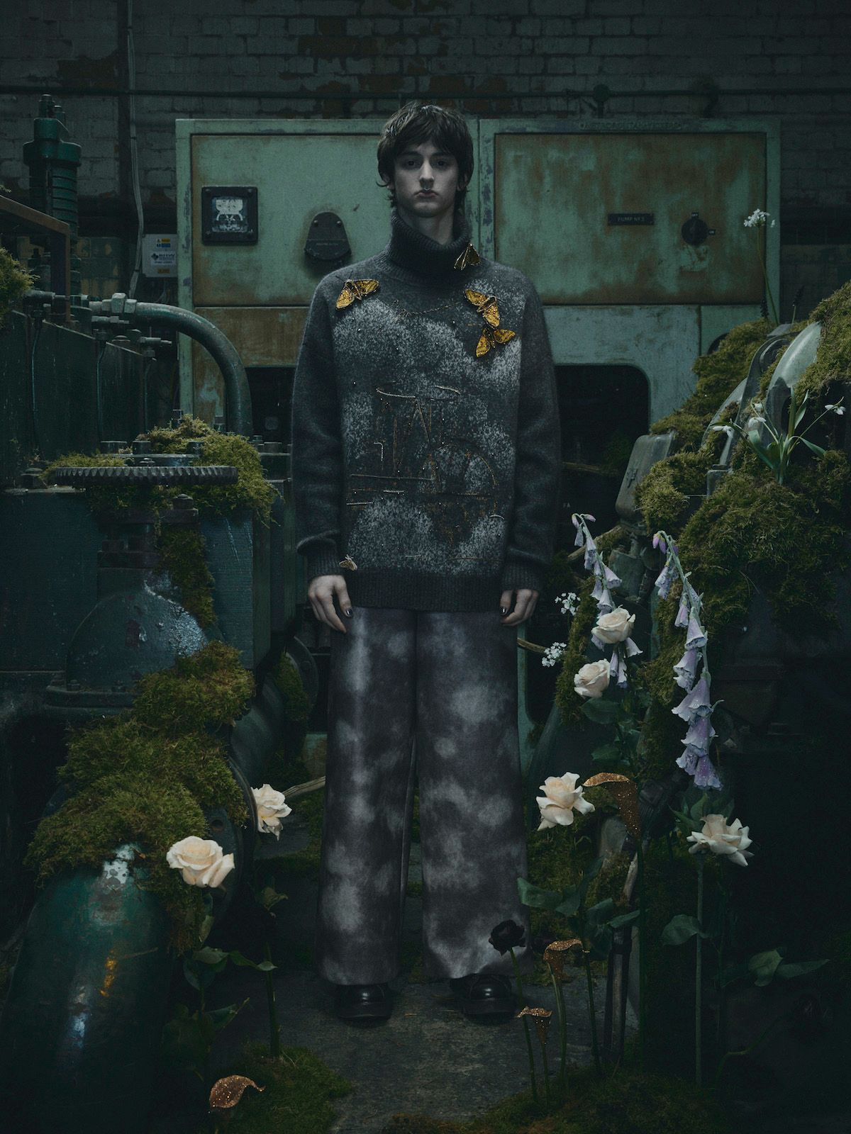 Person in patterned outfit, standing in an overgrown, industrial setting with floral arrangements.