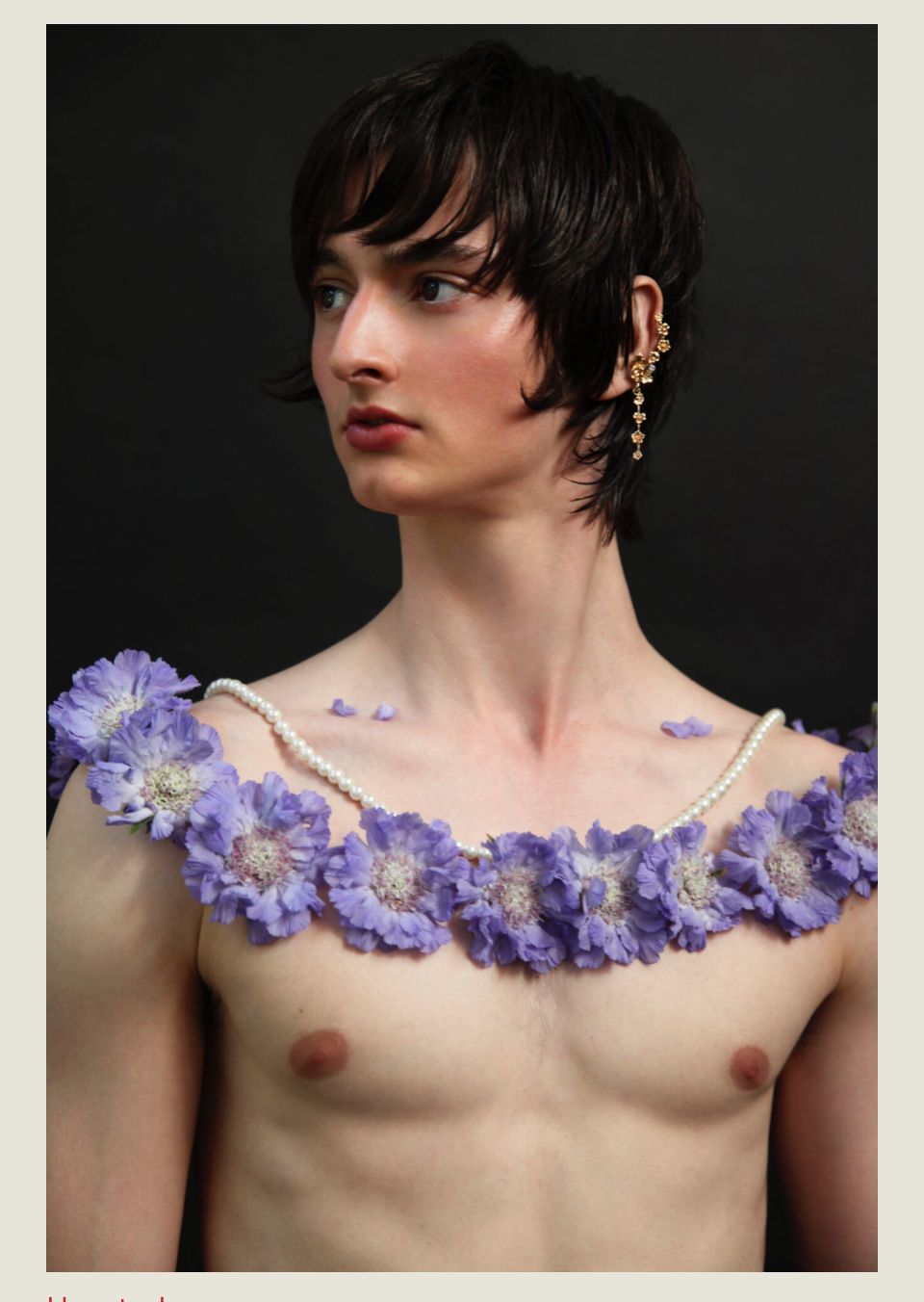 A person with short, dark hair and floral adornment around their neck. They face left.