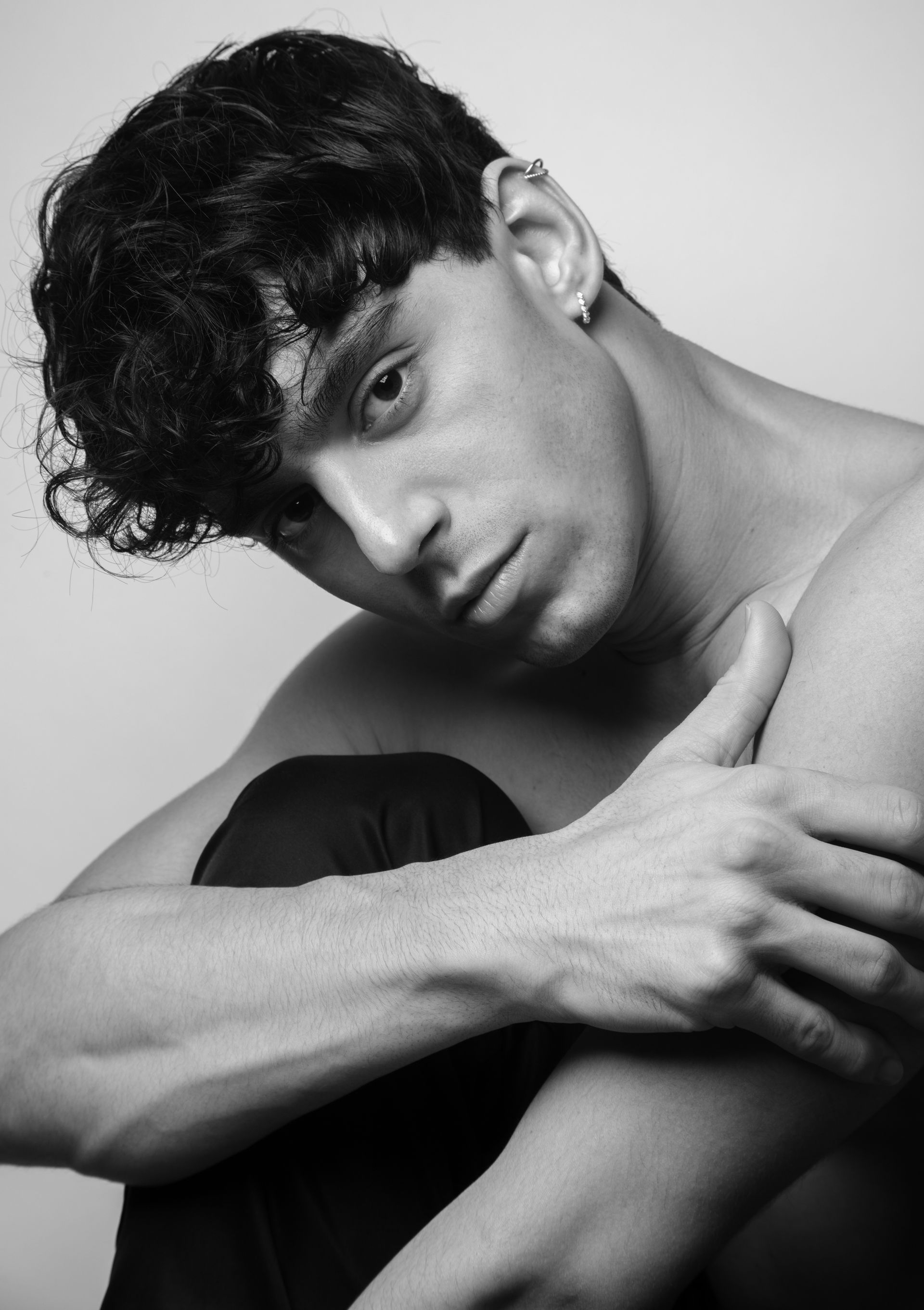 Man with dark curly hair looking at camera, seated with arms crossed. Black and white.