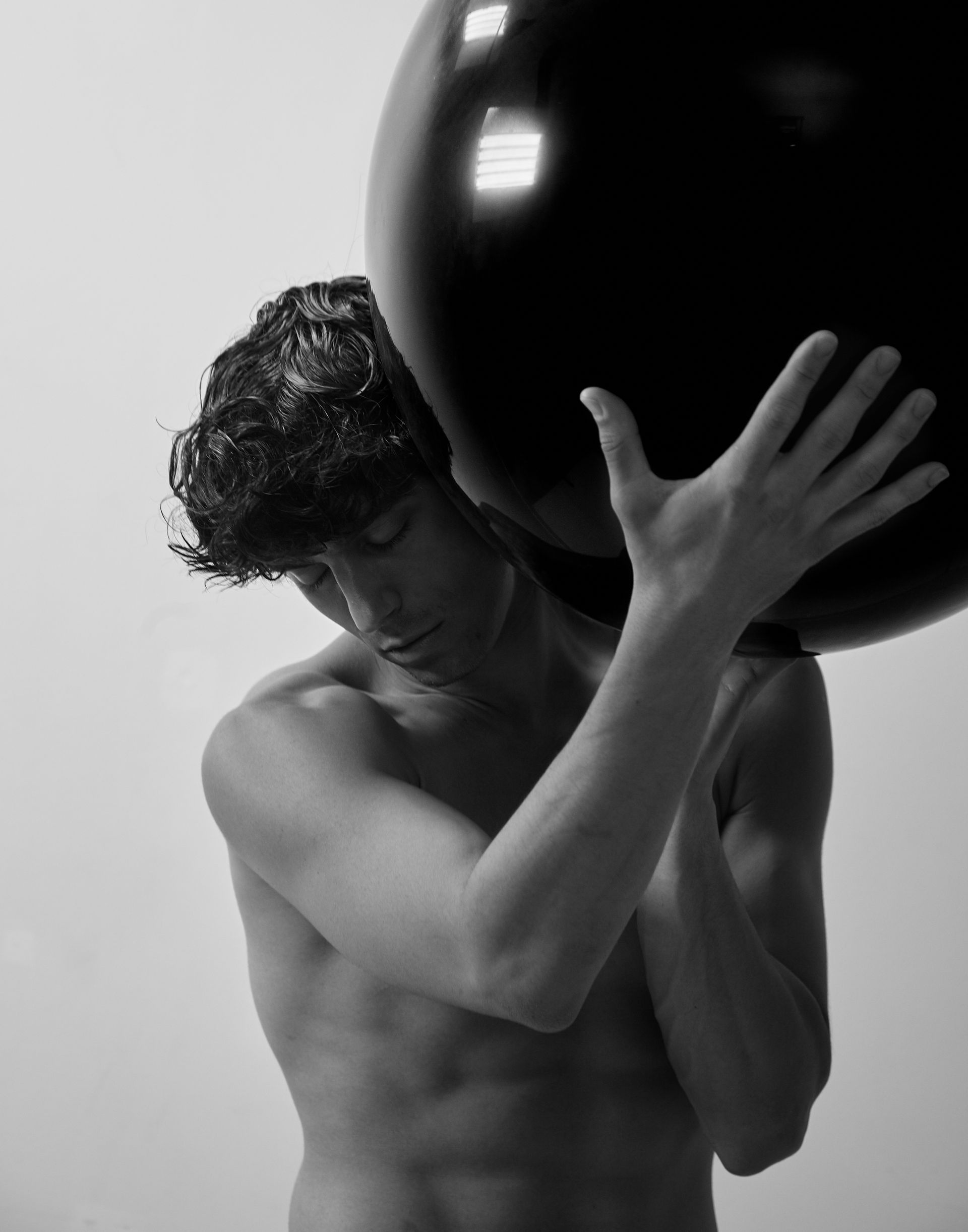Shirtless person holding a large black sphere over their shoulder.