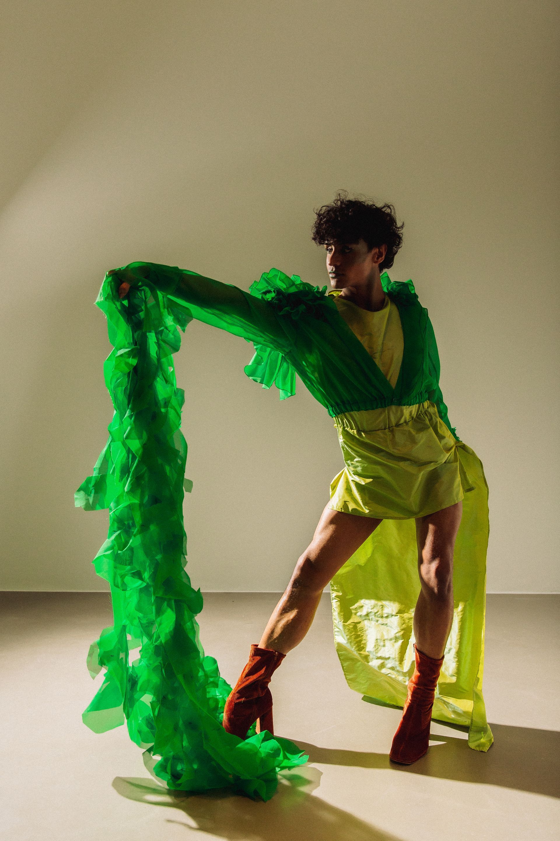 Person in lime and green gown with matching long fabric, brown boots, holding fabric.