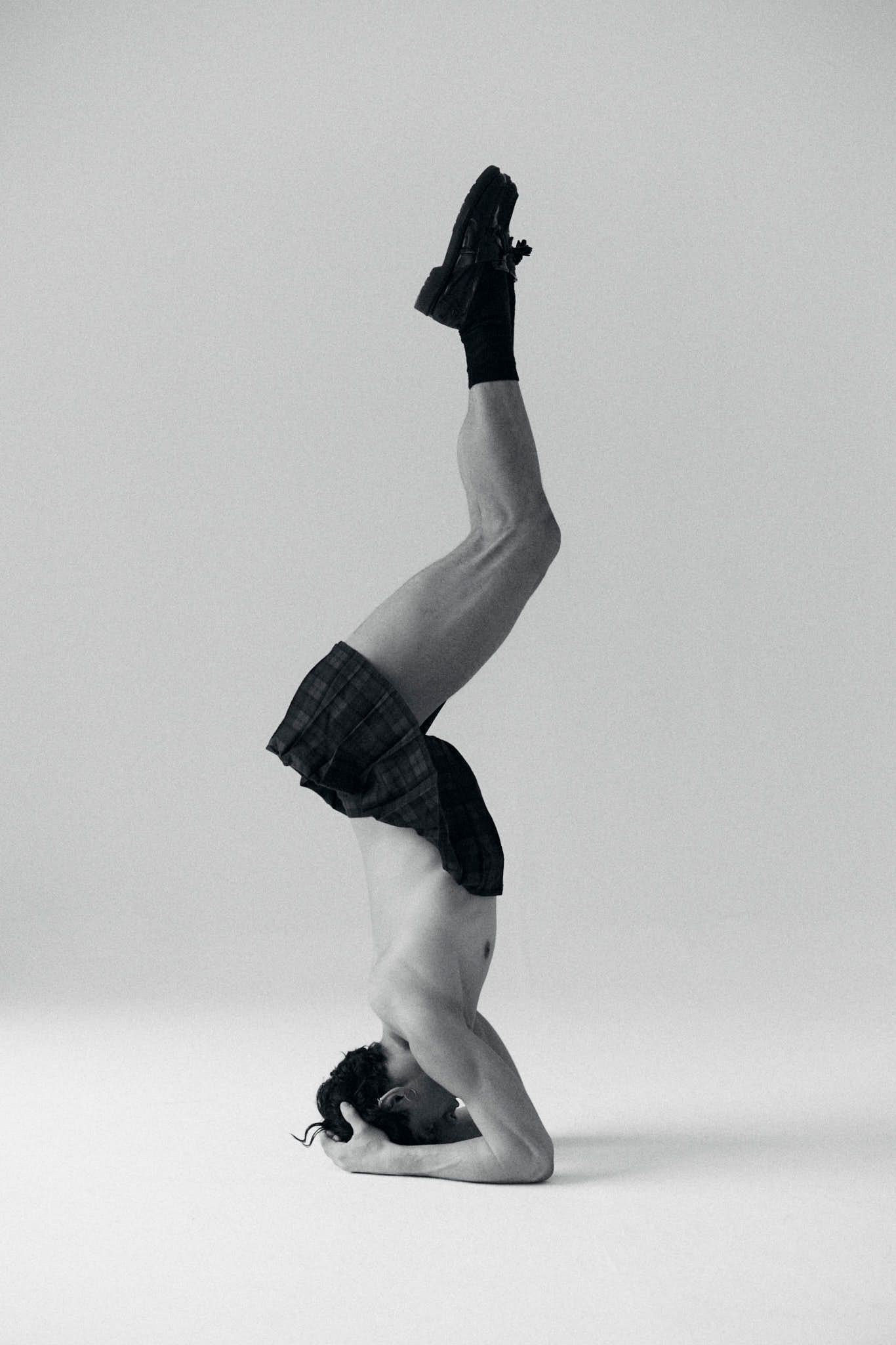 Man in shorts in headstand with one leg bent, socks on. Gray background.
