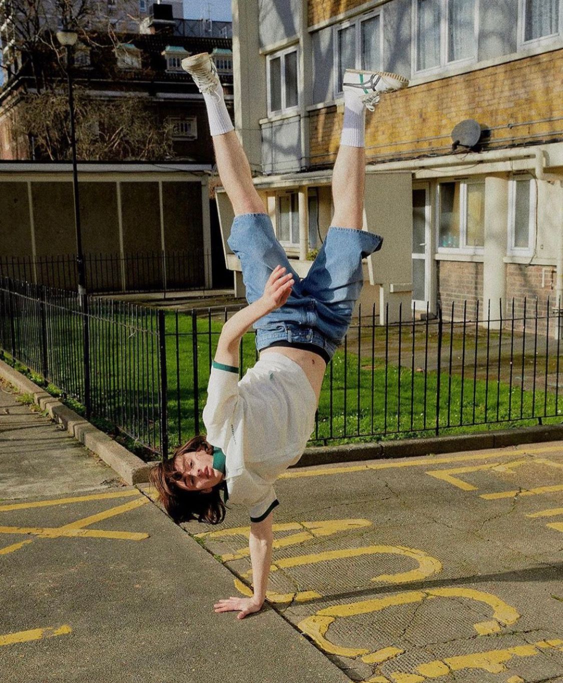 Person doing a handstand on pavement near a building. They wear shorts, shirt, and socks.
