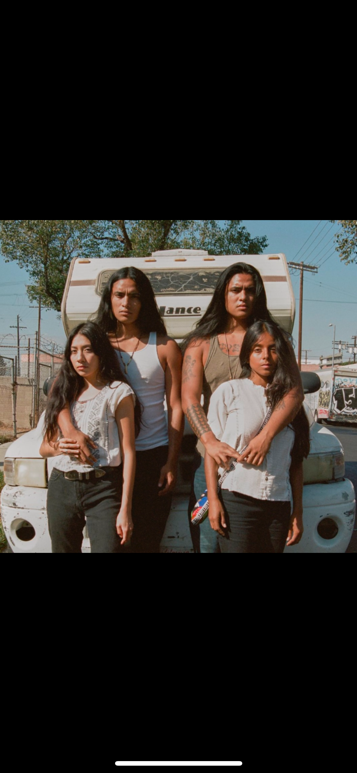 Four people in front of a camper. Two hug each other while others stand in front.