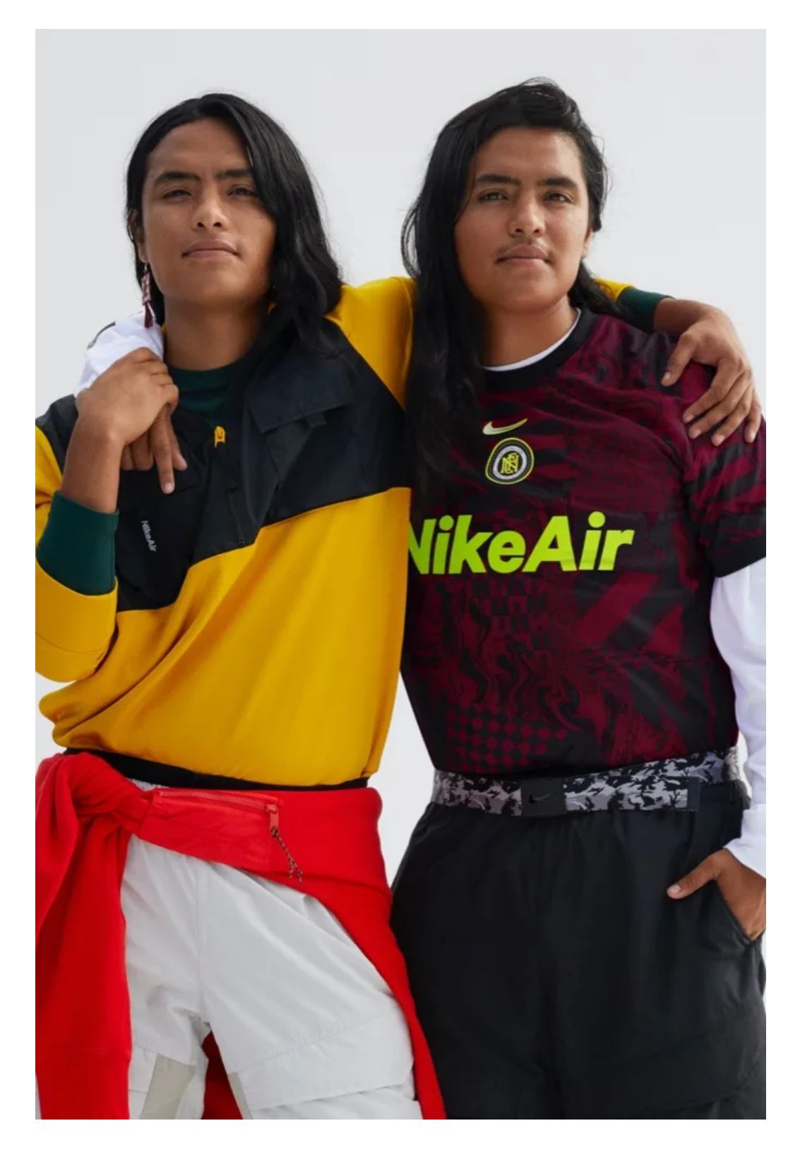 Two people with long hair in Nike clothing posing together, one with an arm around the other.