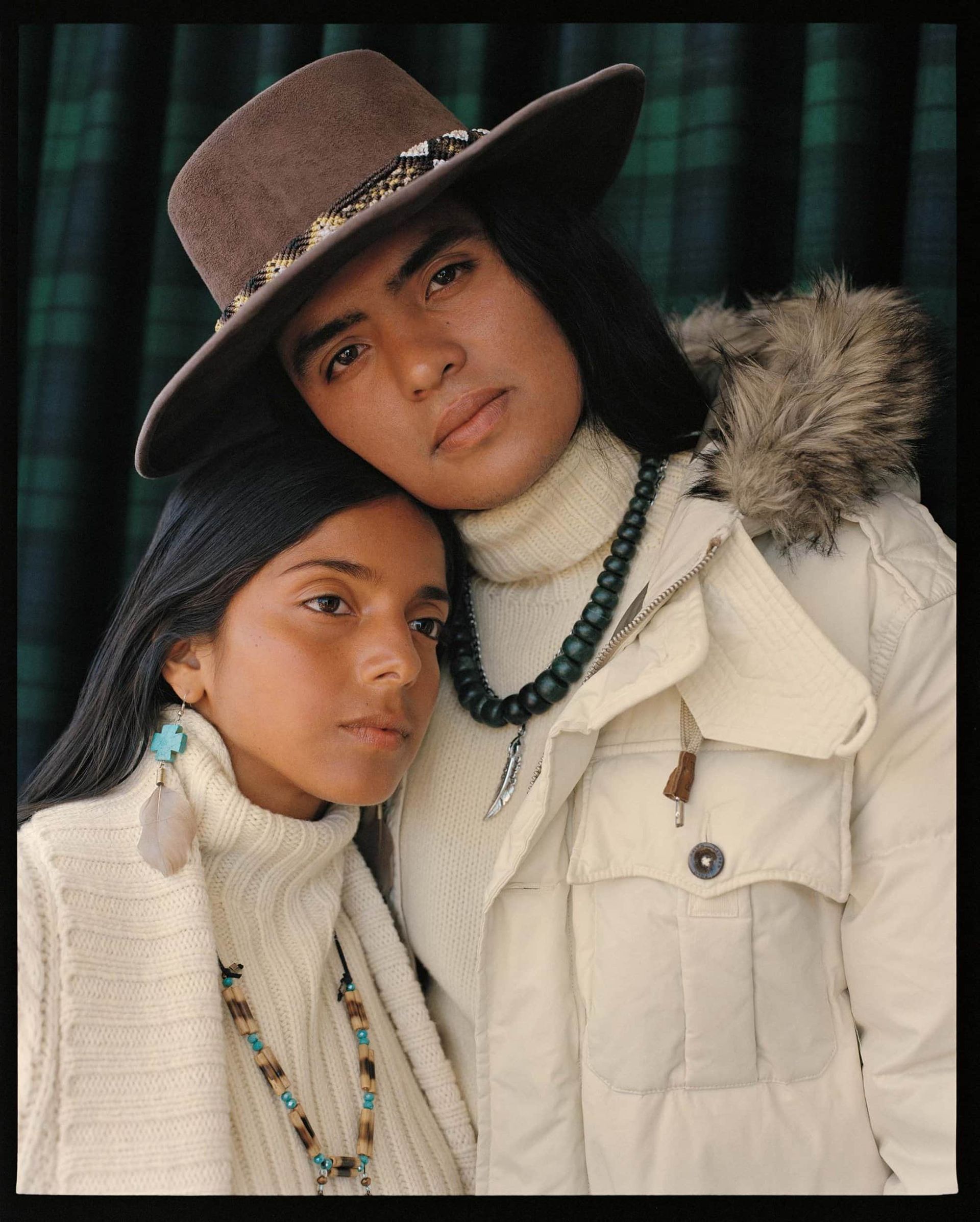 Couple in cream-colored turtlenecks and jacket, leaning on each other. The person on the right is wearing a brown hat.