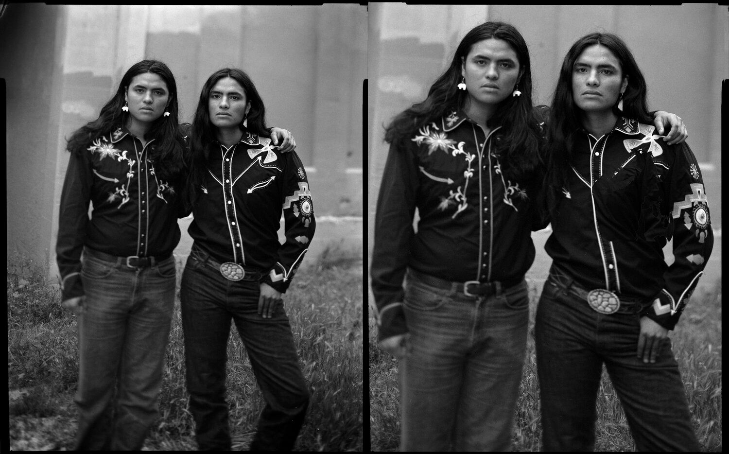 Two people in matching embroidered shirts and jeans, standing near a wall and grassy area.
