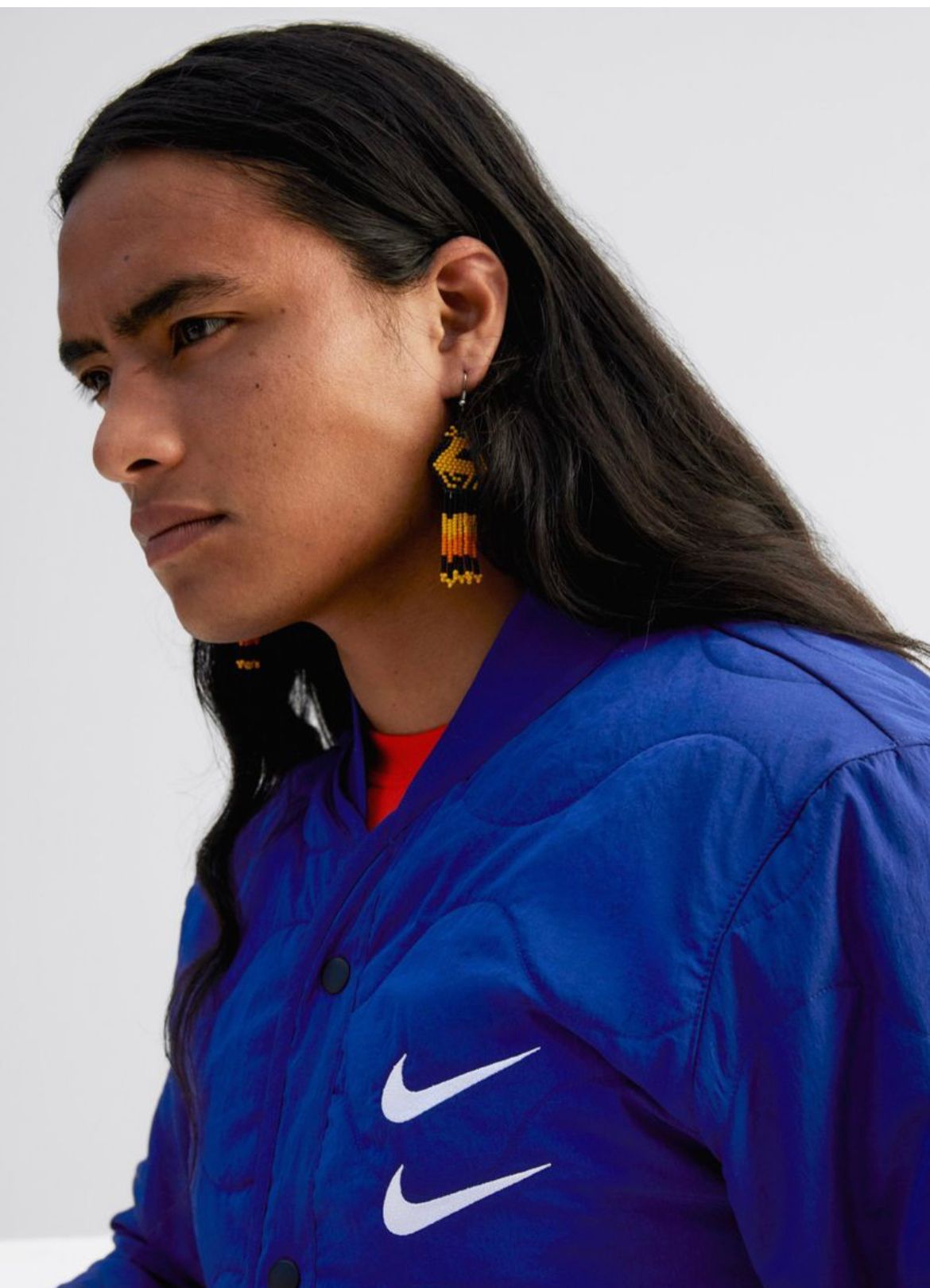 Person with long dark hair wearing a blue jacket with a double white Nike swoosh.