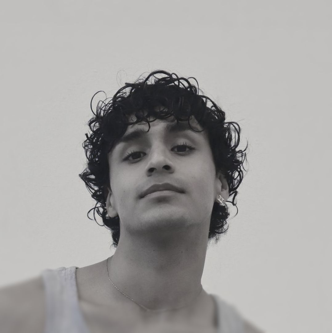 Man with curly dark hair looking at the camera, wearing a tank top. Black and white photo.