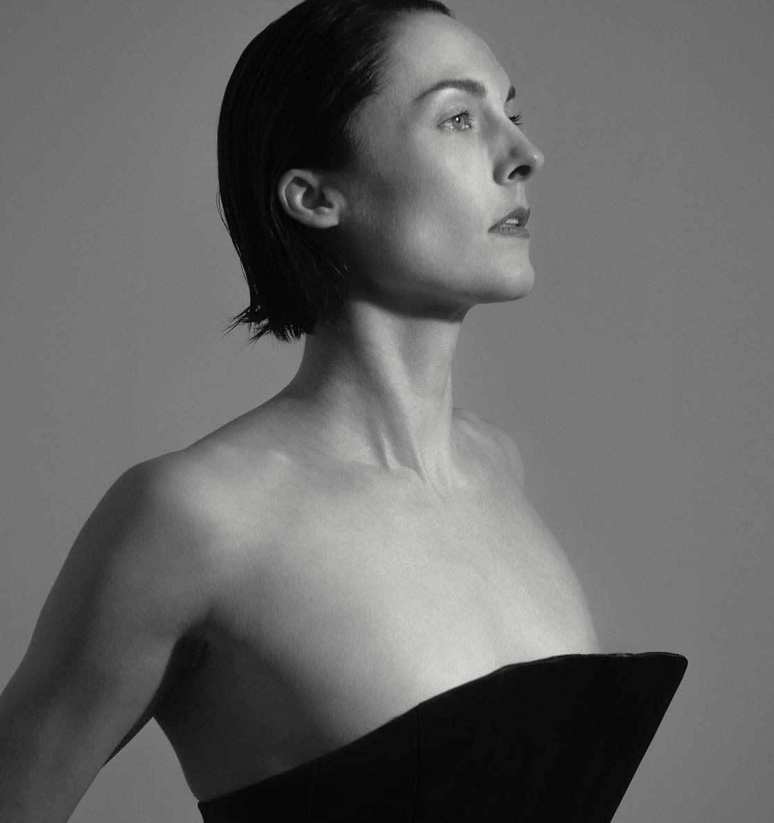 Woman in strapless black top looking upward. Black and white, studio setting.