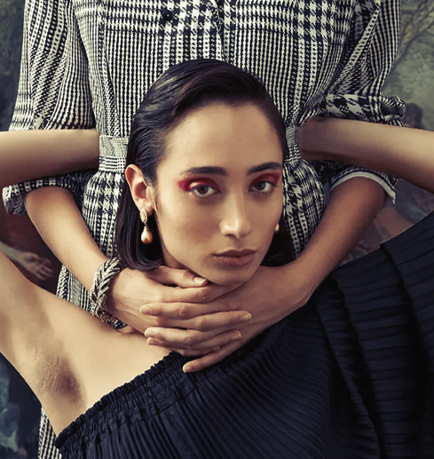 Woman in dark dress, arms around neck by person in plaid, red eyeshadow, gold earrings.