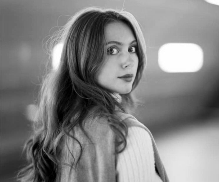 Woman with long hair looking over her shoulder, wearing a sweater, lit by ambient lighting.