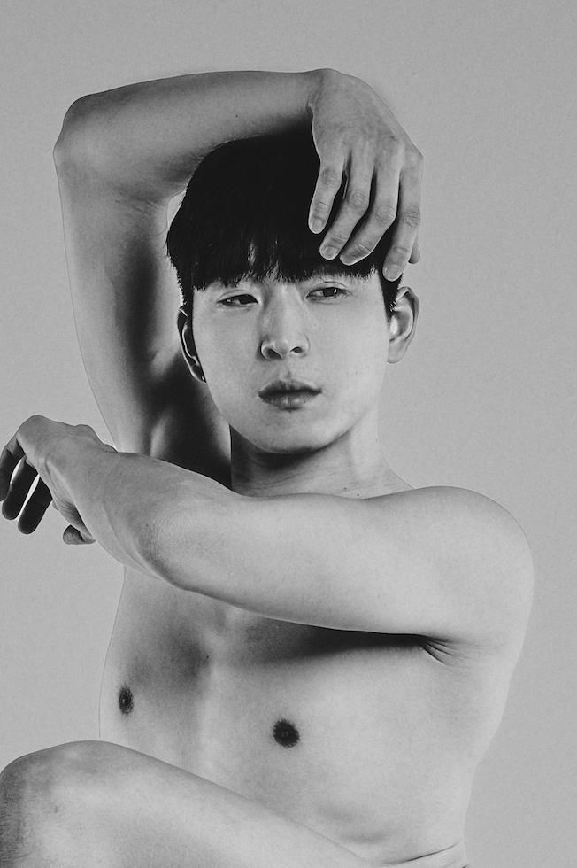 Shirtless person with arm raised, looking at the camera. Black and white.