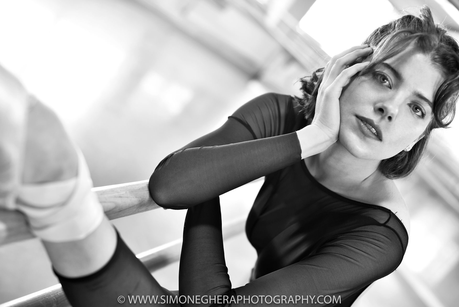 Ballet dancer resting, leaning on a bar, looking at the camera. Black and white.