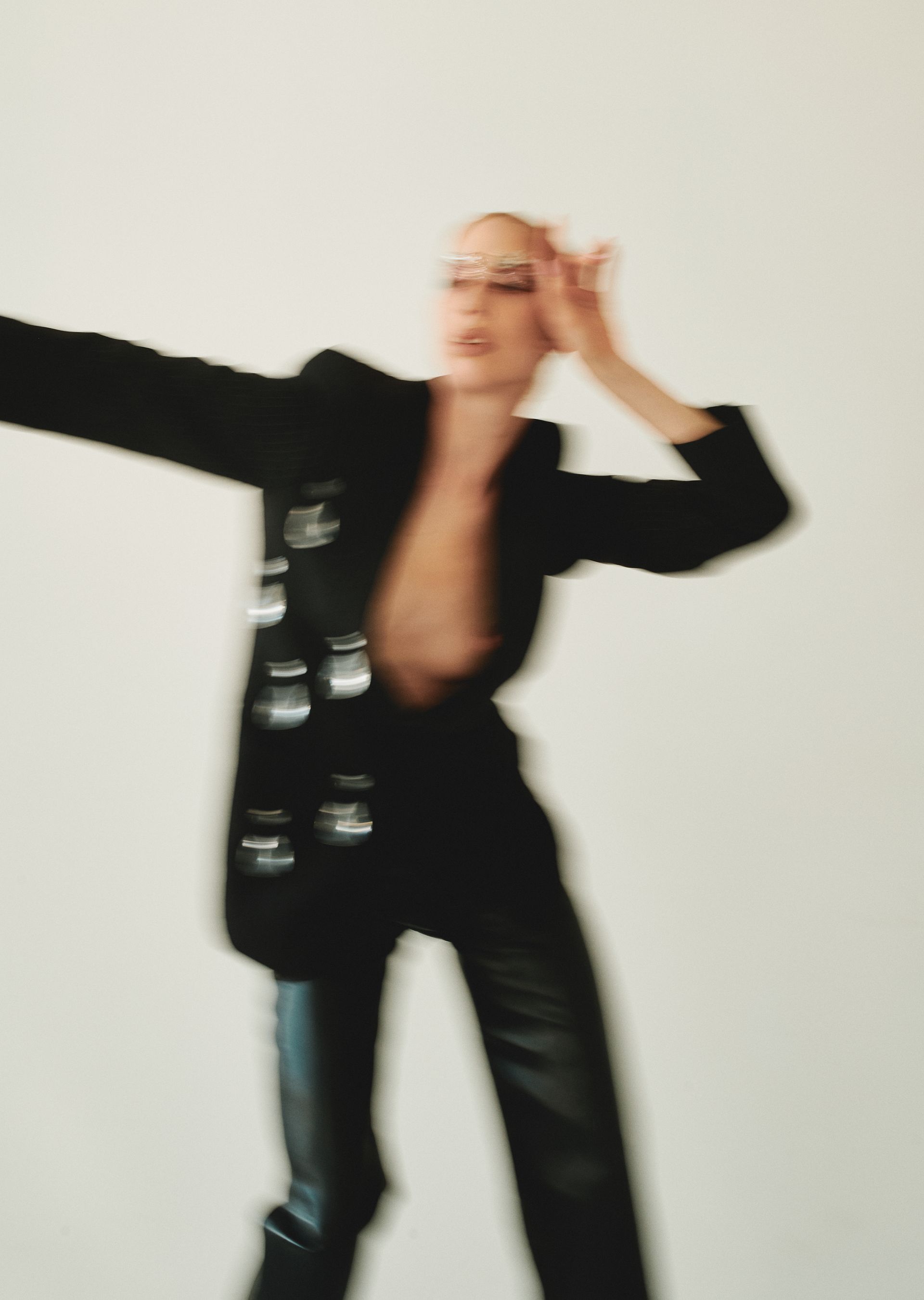 Woman in black blazer and pants, hands up, blurred motion, white background.