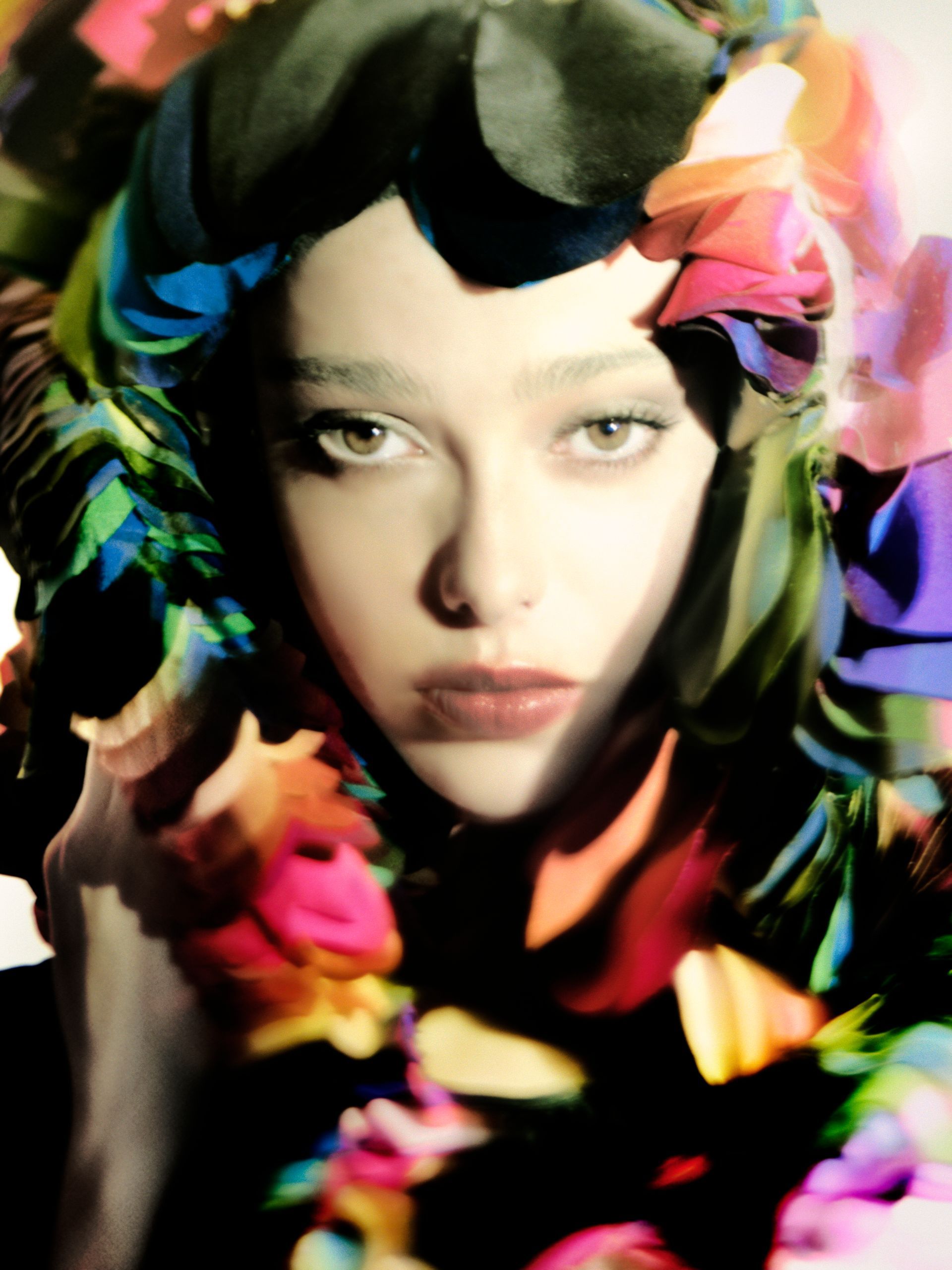 Woman with pale skin, framed by colorful fabric and flowers, looking forward.