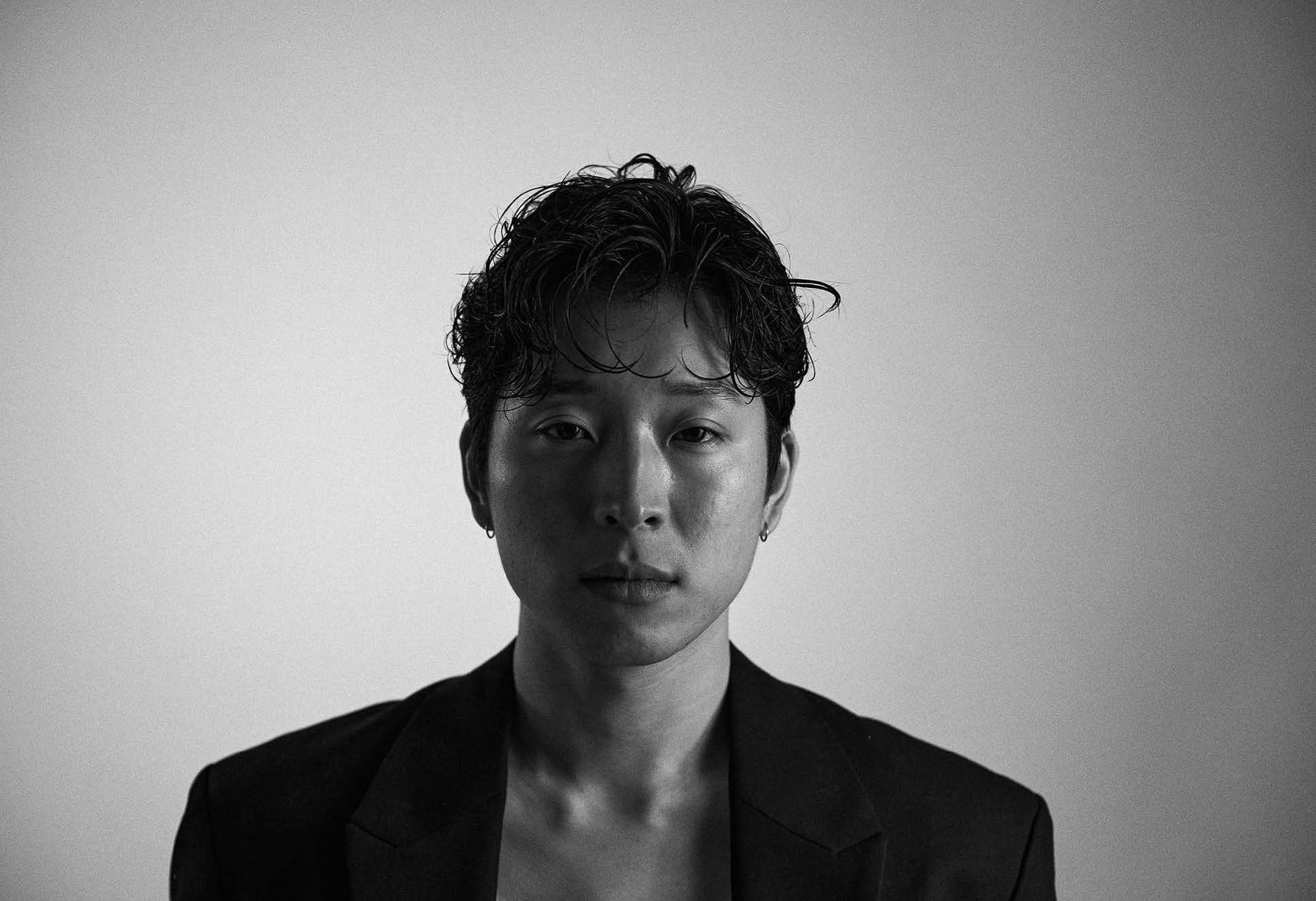 A person with curly hair and a blazer, looking at the camera in a black and white photo.