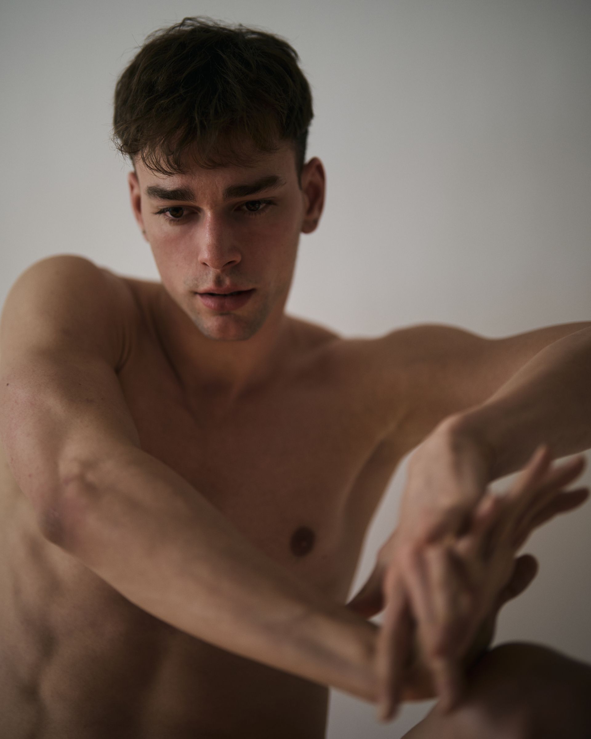 A person with short, dark hair looking forward, with arms crossed, next to another person with their arm raised.