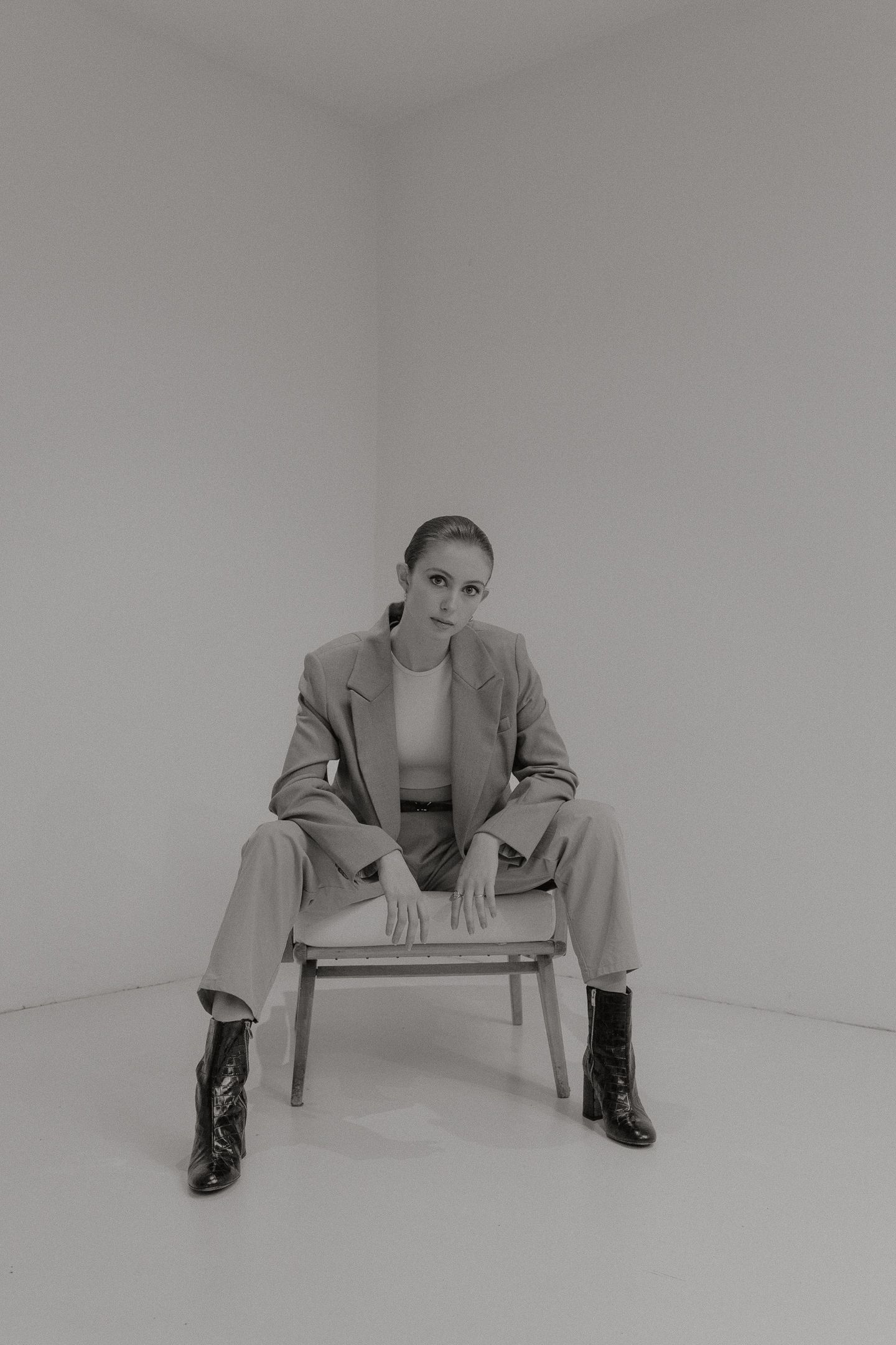 Woman seated in a chair, wearing a suit and boots, with a neutral expression. Black and white photo.