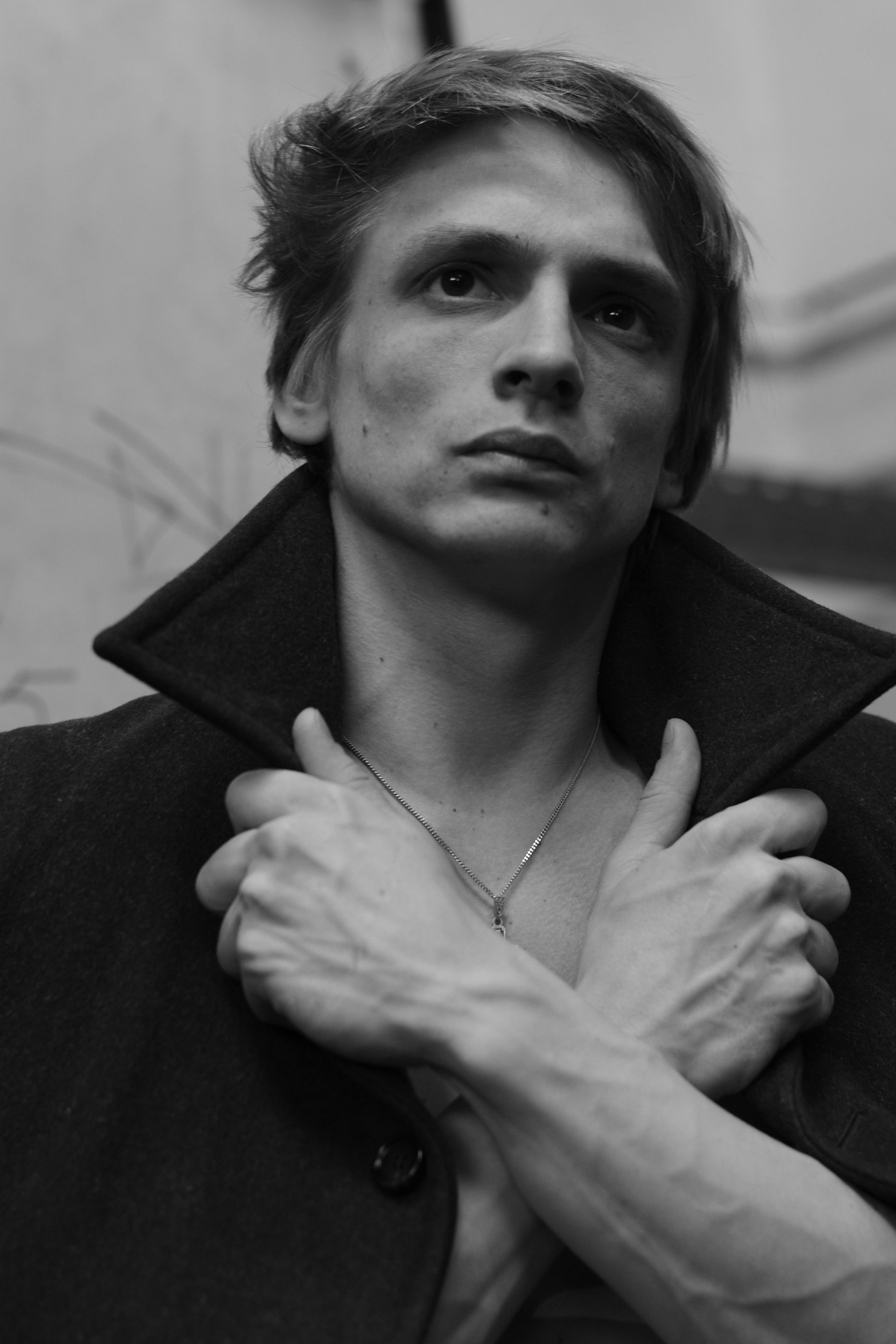 Man in dark coat with crossed arms, looking up. Black and white photo.