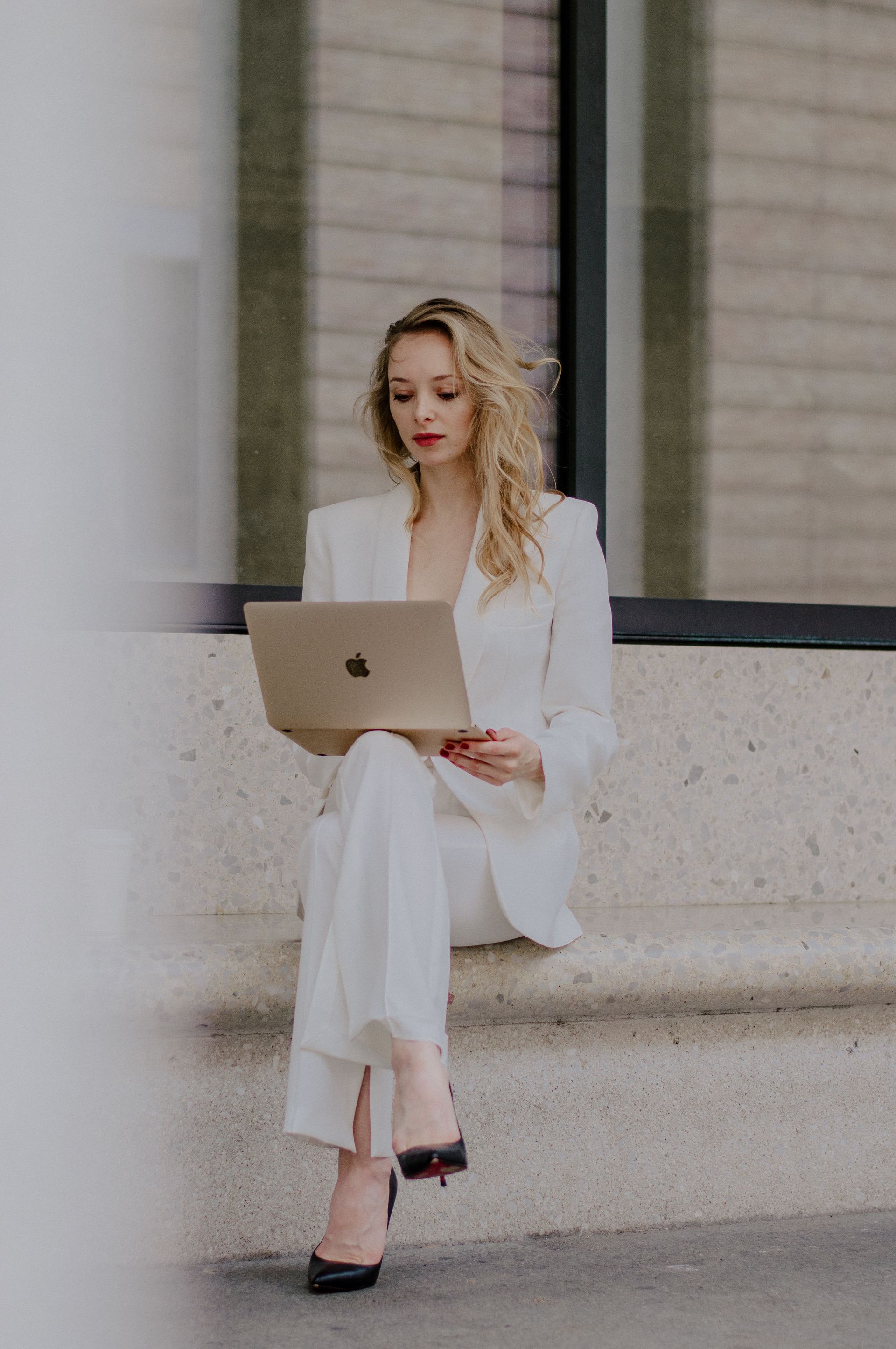 Woman in white suit works on laptop, sitting outdoors.