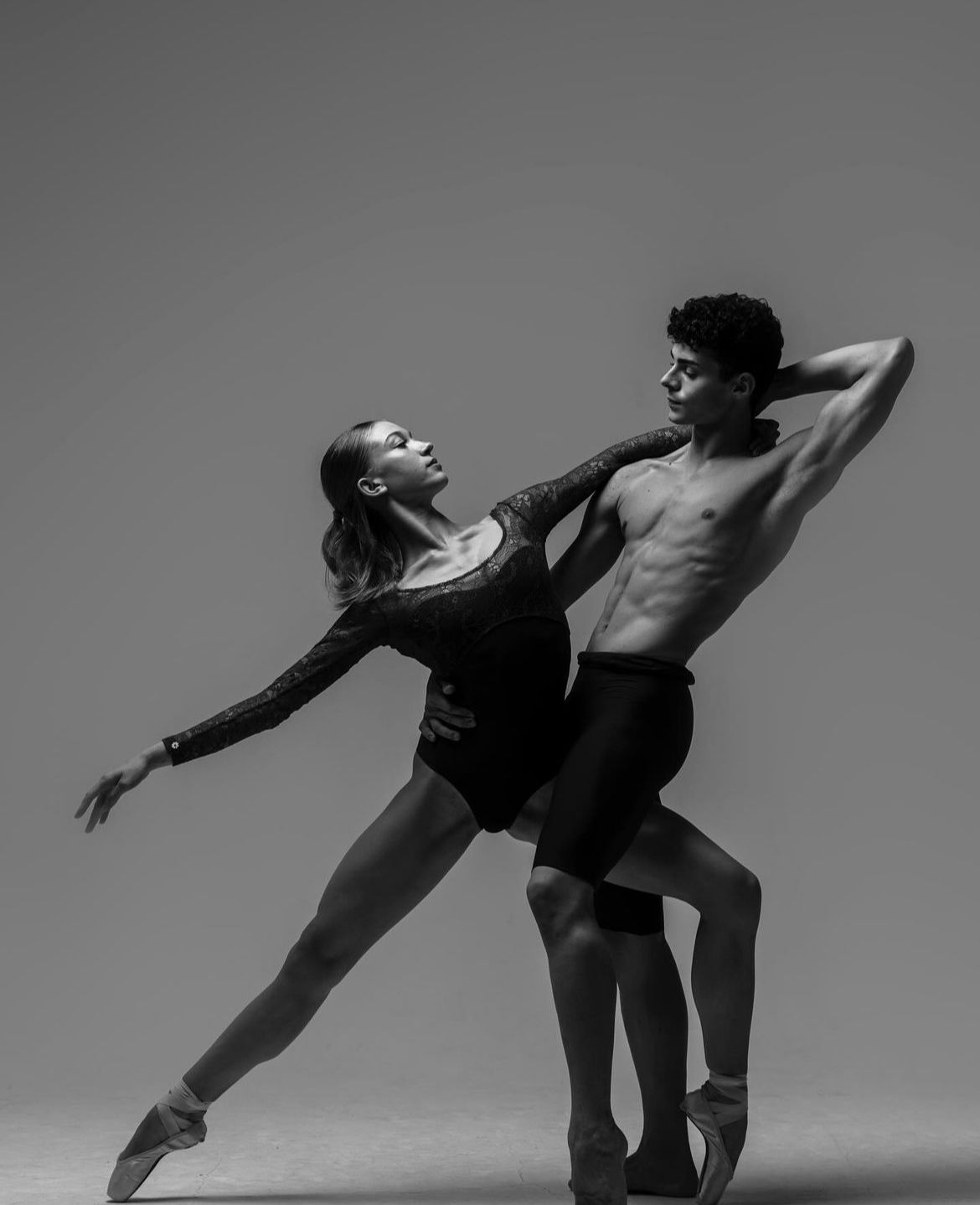 Ballet dancers in graceful pose, woman in leotard, man shirtless, performing in studio.