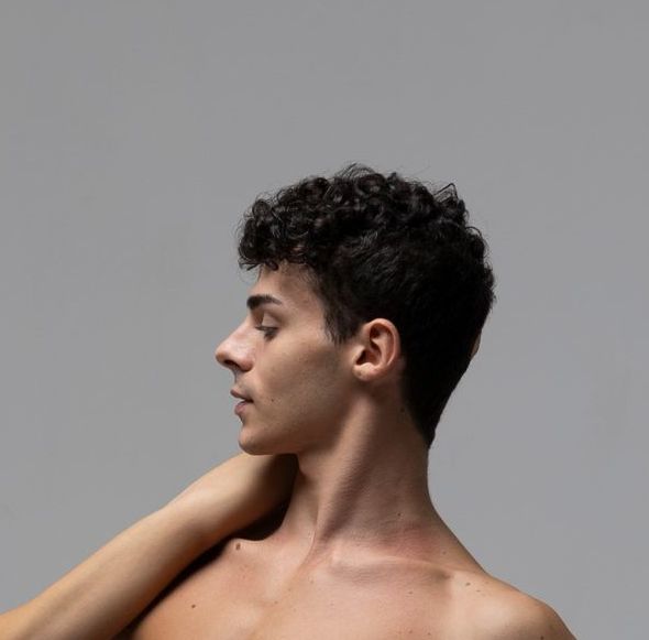 Man with dark curly hair looking to the side; arm raised near shoulder, chest exposed.