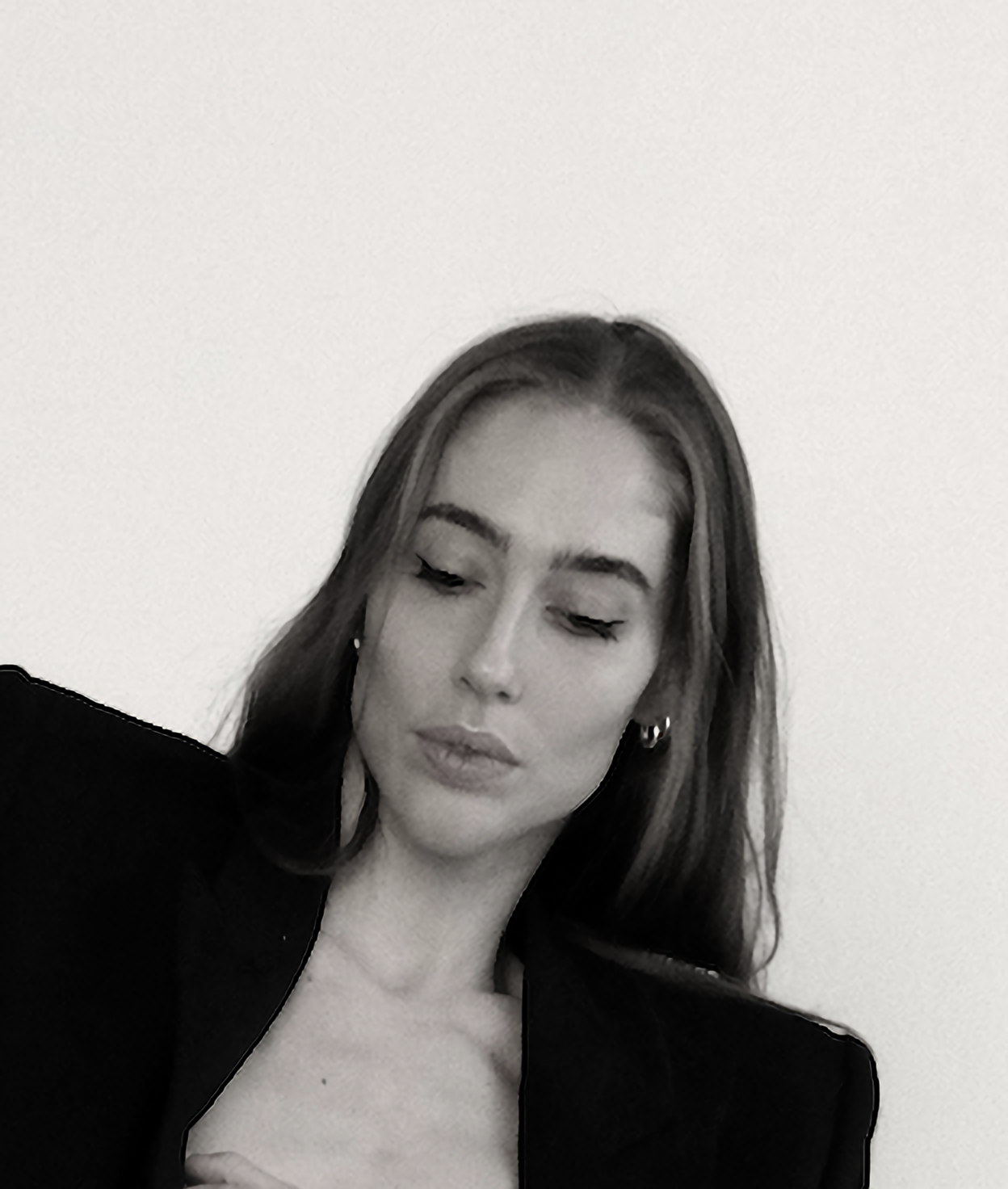 Woman wearing a blazer, looking down with a neutral expression against a white backdrop.