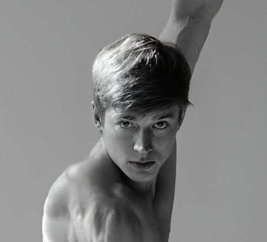 Man with tousled hair looking forward, arm raised. Black and white photo.