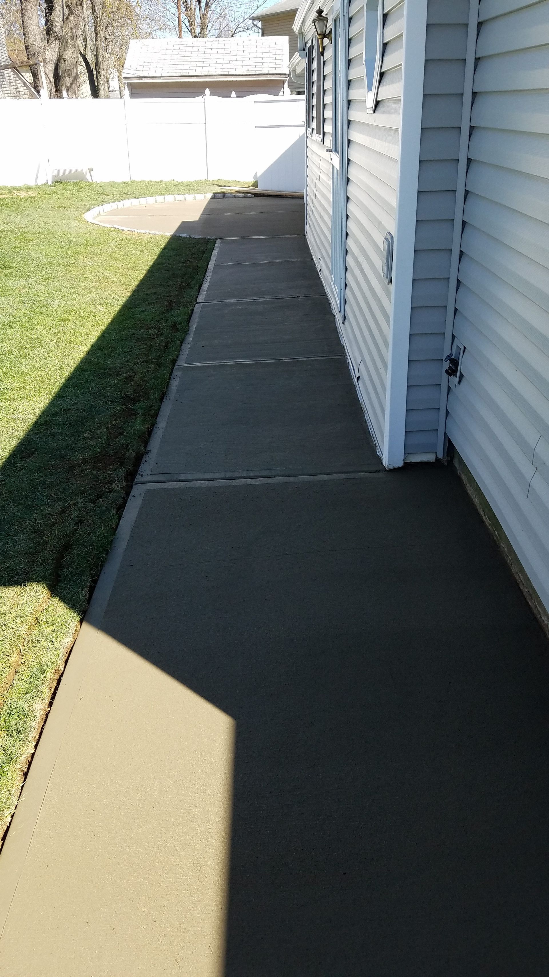 Concrete walkway alongside a light blue house, with green grass to the left.