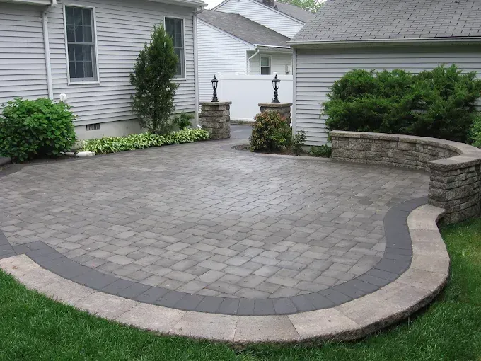 Brick patio with curved border, small retaining wall, and surrounding grass.