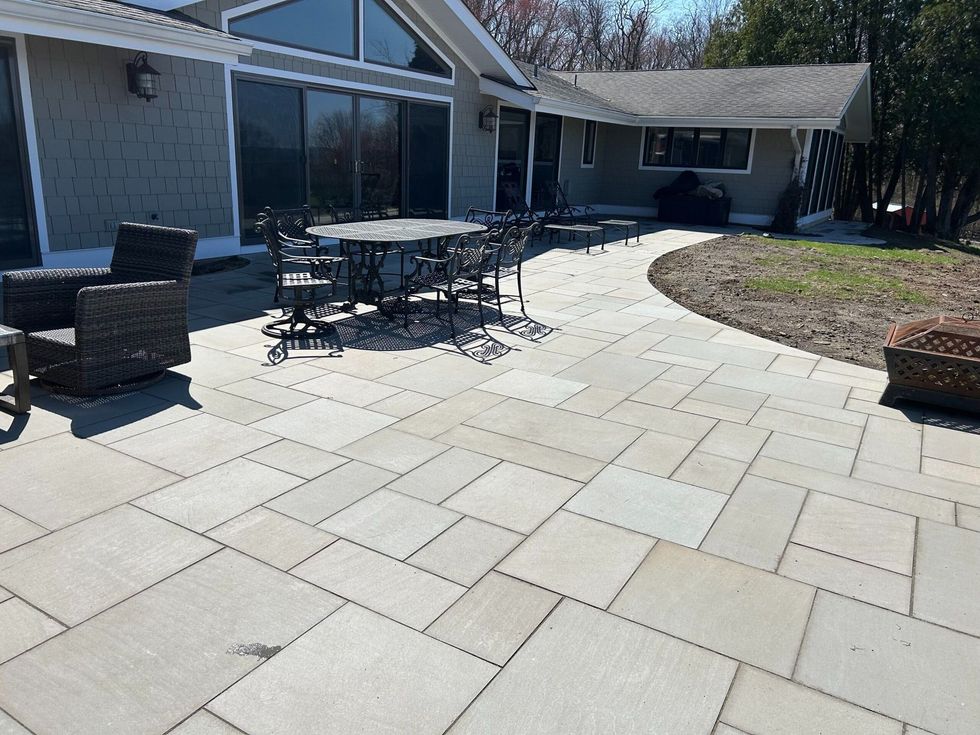 Patio with stone pavers, outdoor furniture, and a house in the background.