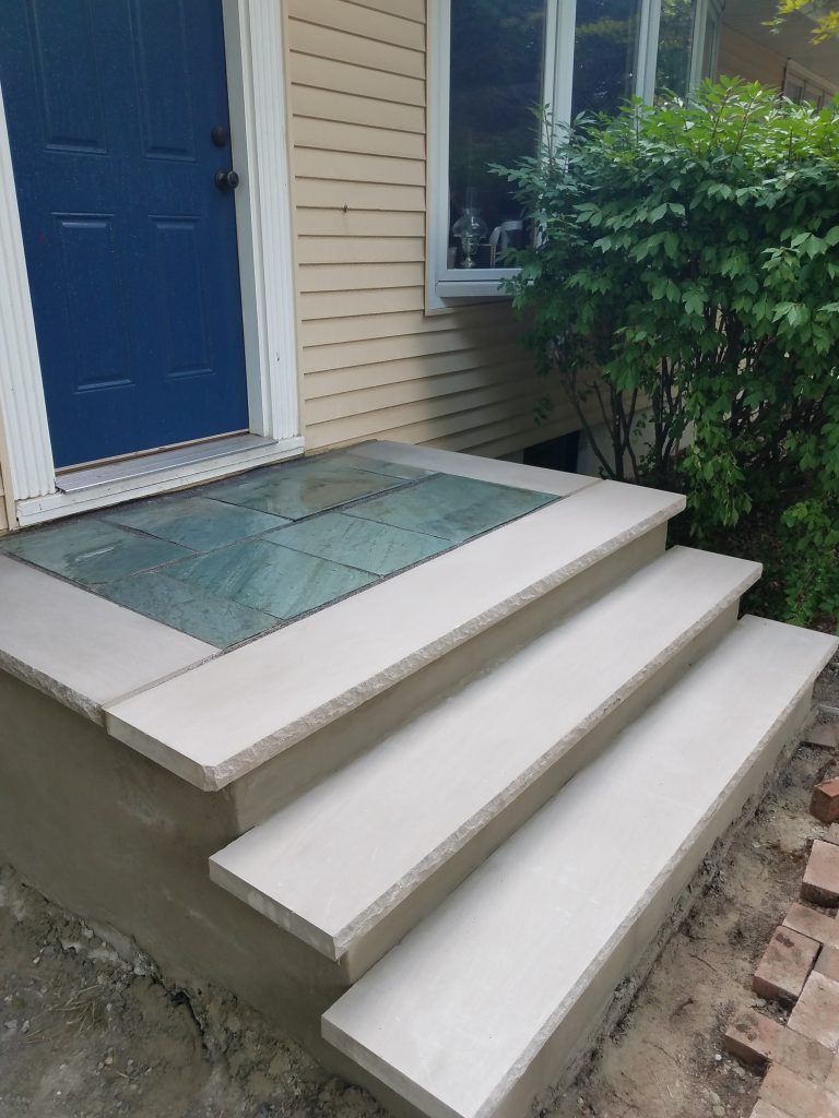 Blue door with three light-colored steps leading up to a covered entrance. Beige siding.