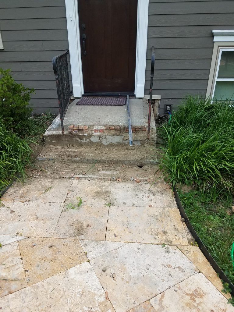 A stone walkway leads to a front door with a crumbling brick and concrete step. Green grass flanks the path.