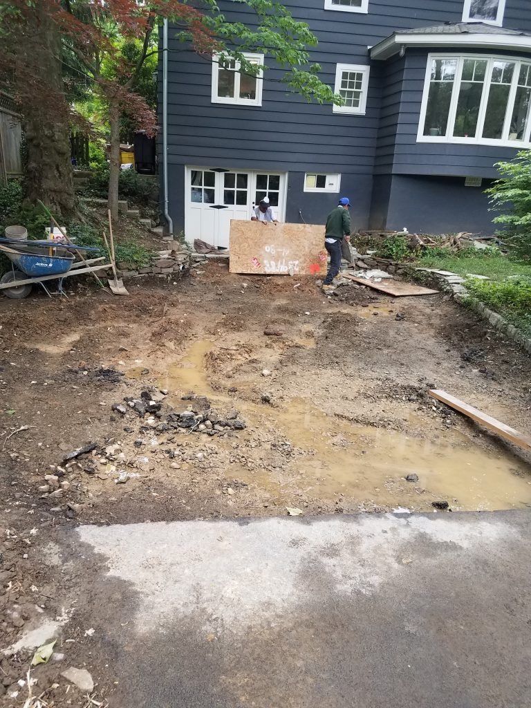 Muddy yard under construction; workers, house with white trim, wooden boards, dark blue siding.